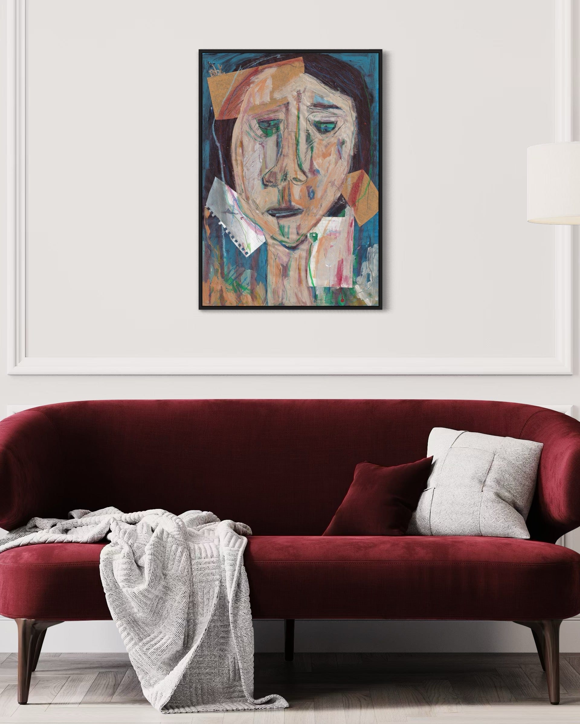 Red sofa with a white blanket and gray pillow, framed abstract art above on a white wall.