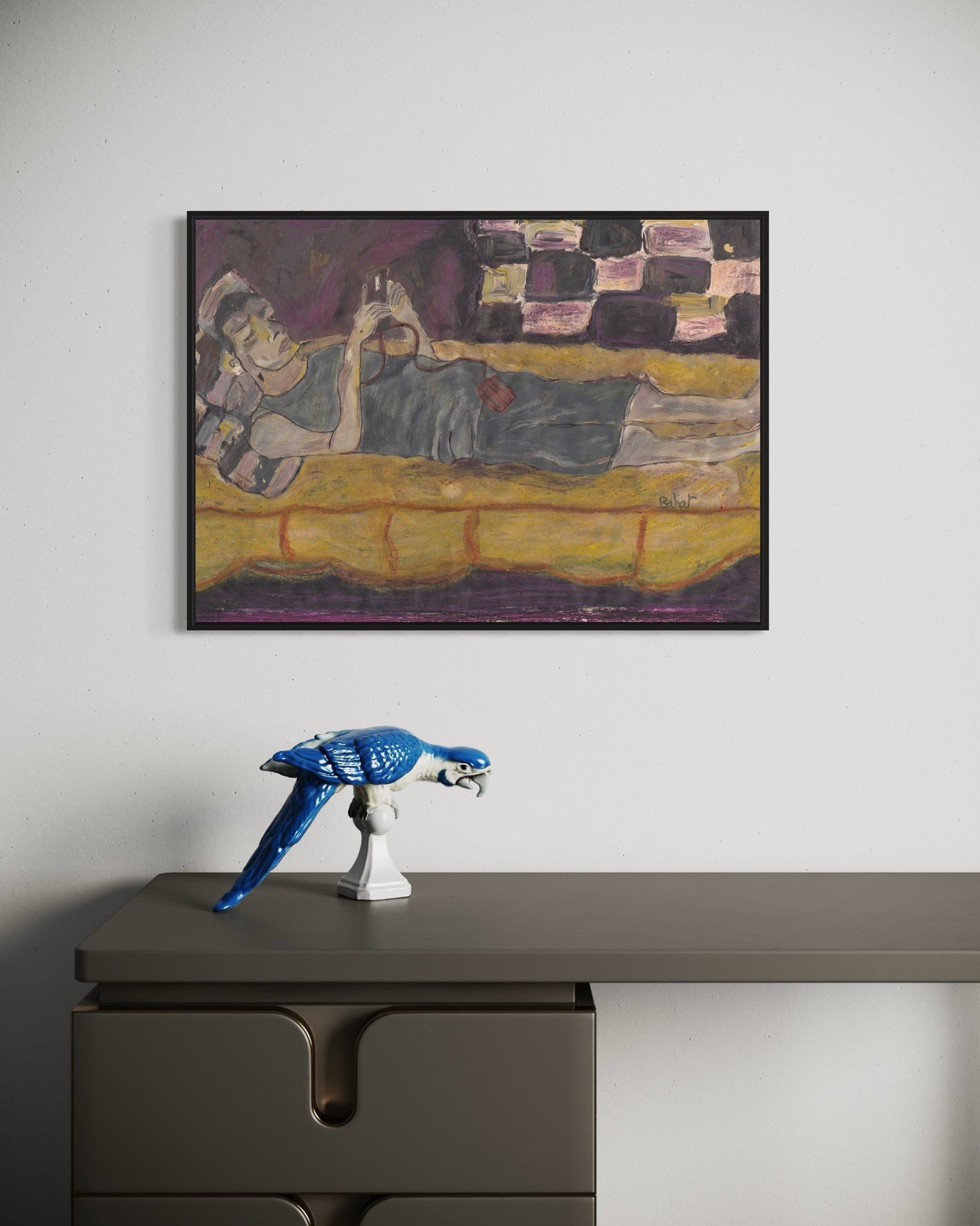 Framed painting of a reclining figure on a yellow couch above a desk with a blue sculpture.
