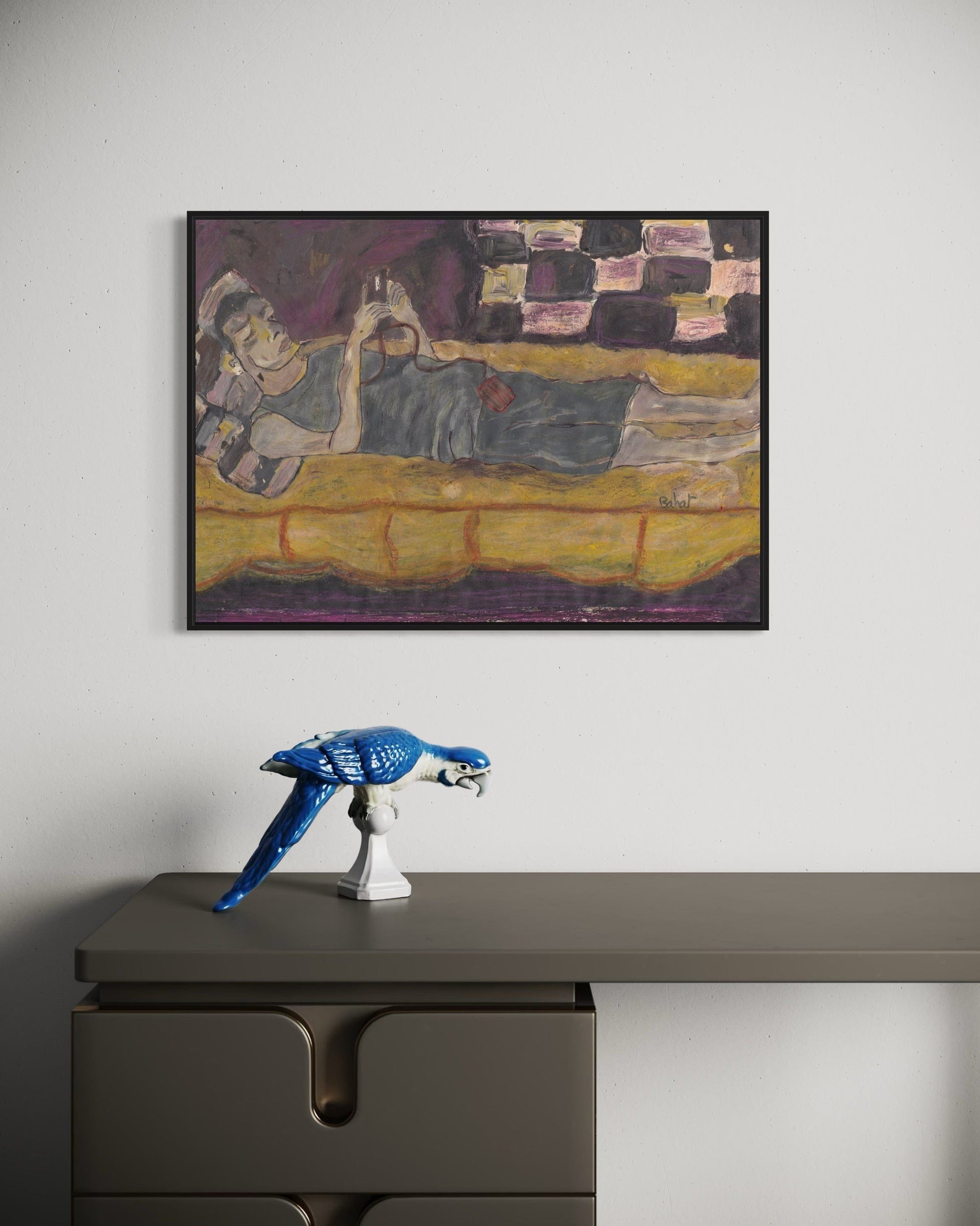 Framed painting of a reclining figure on a yellow couch above a desk with a blue sculpture.