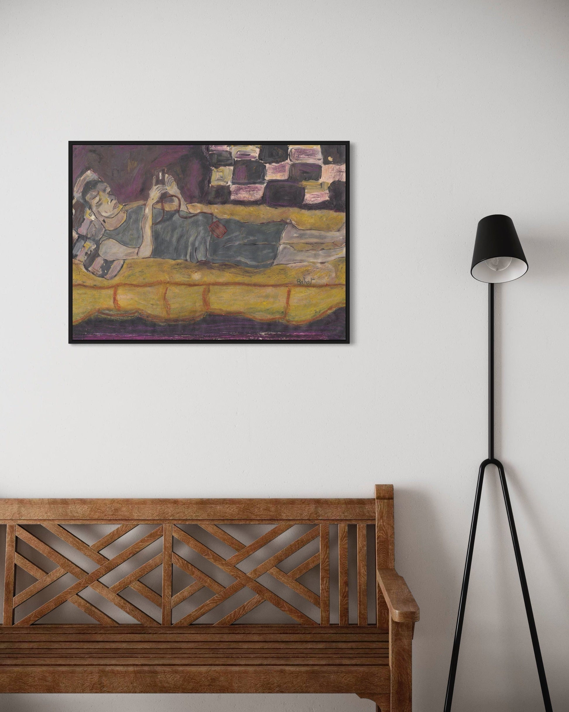 Framed artwork on a wall above a wooden bench with a black floor lamp to the right.