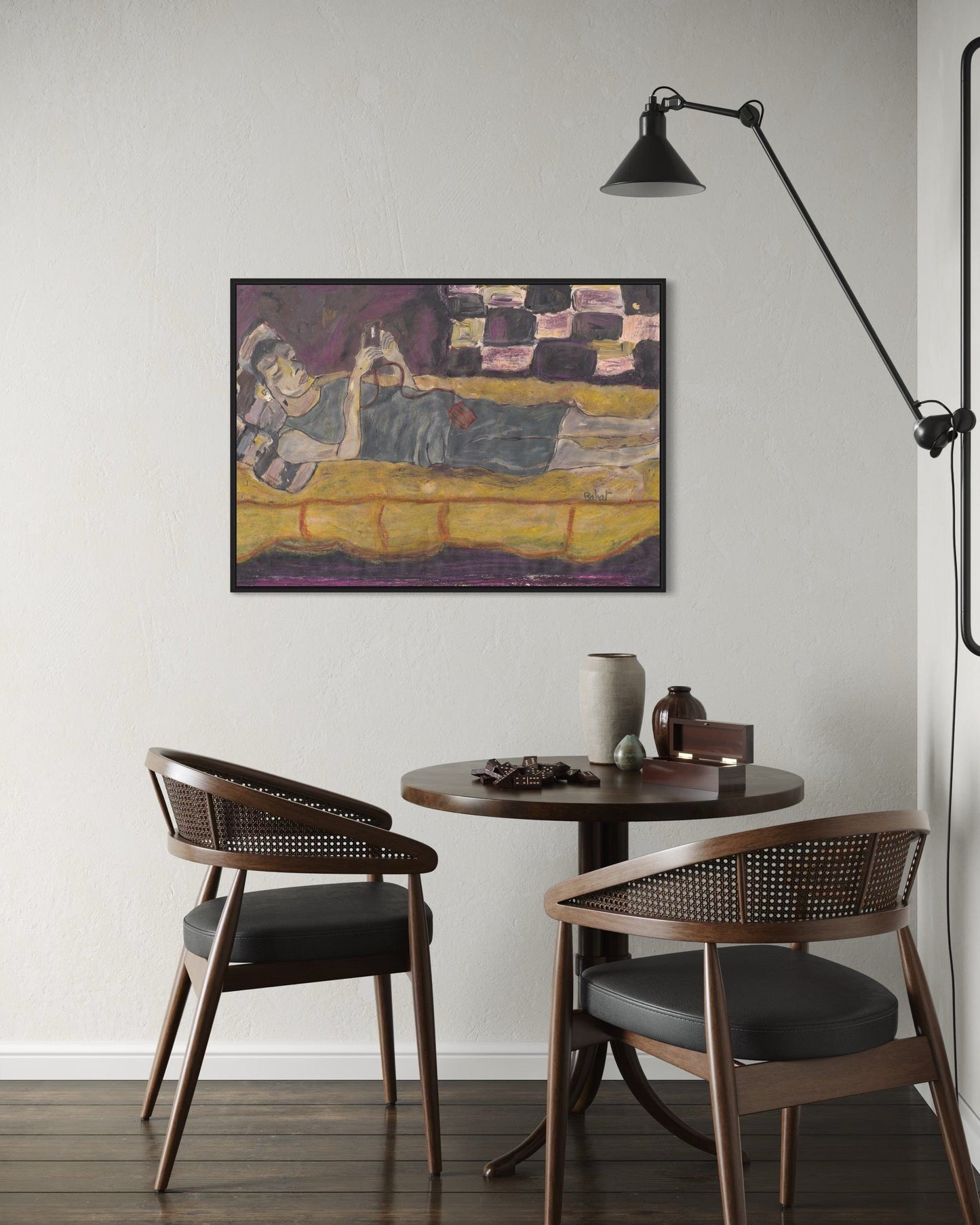 Small dining area with round table and two chairs, featuring a wall-mounted lamp and framed artwork.