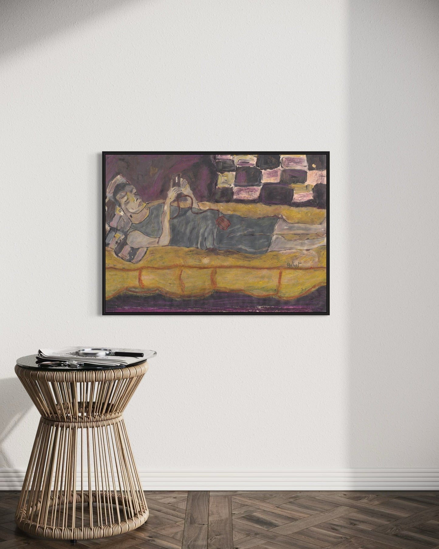 Framed painting of a reclining figure on a yellow couch above a wicker side table.