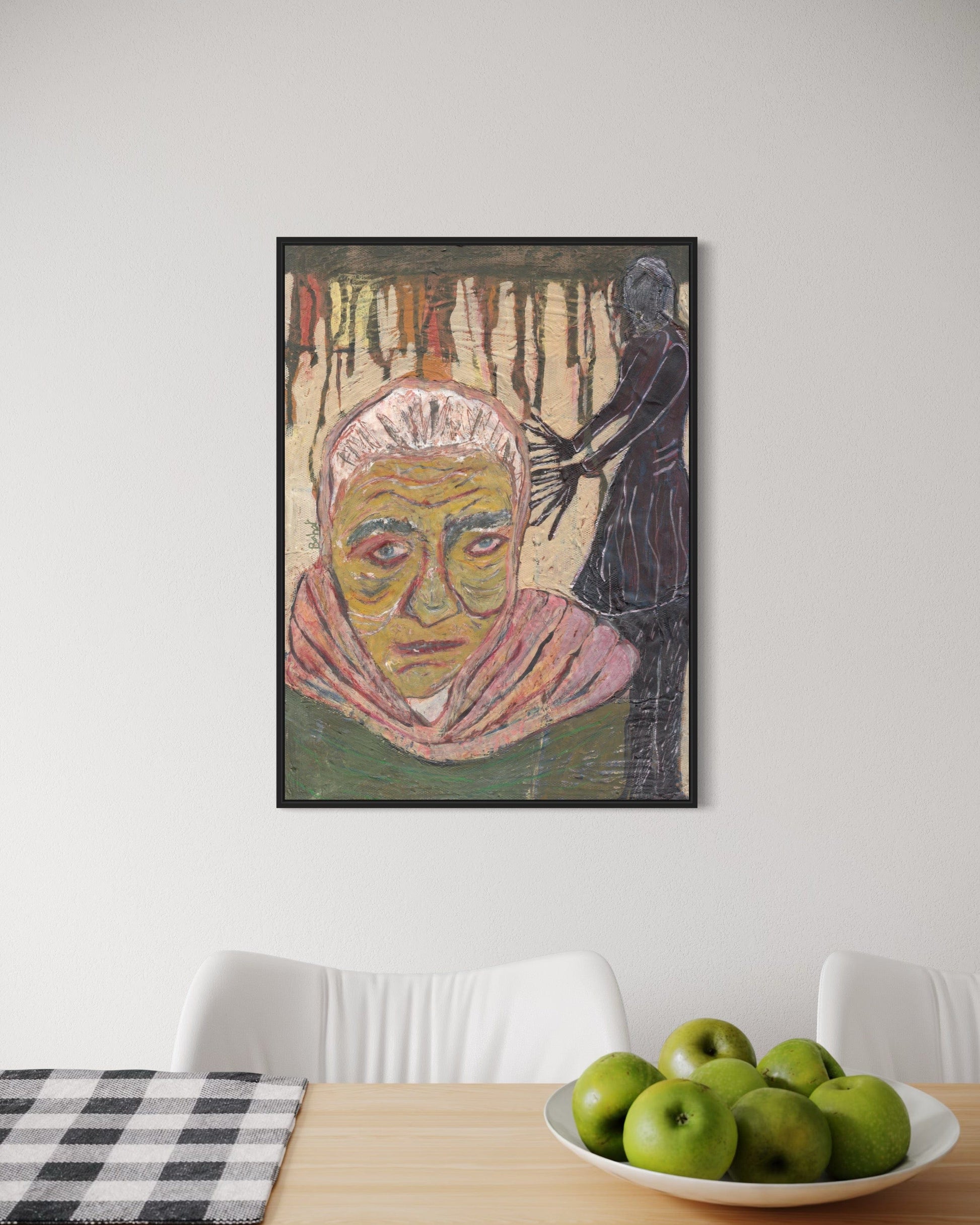 Framed artwork on a wall above a table with apples