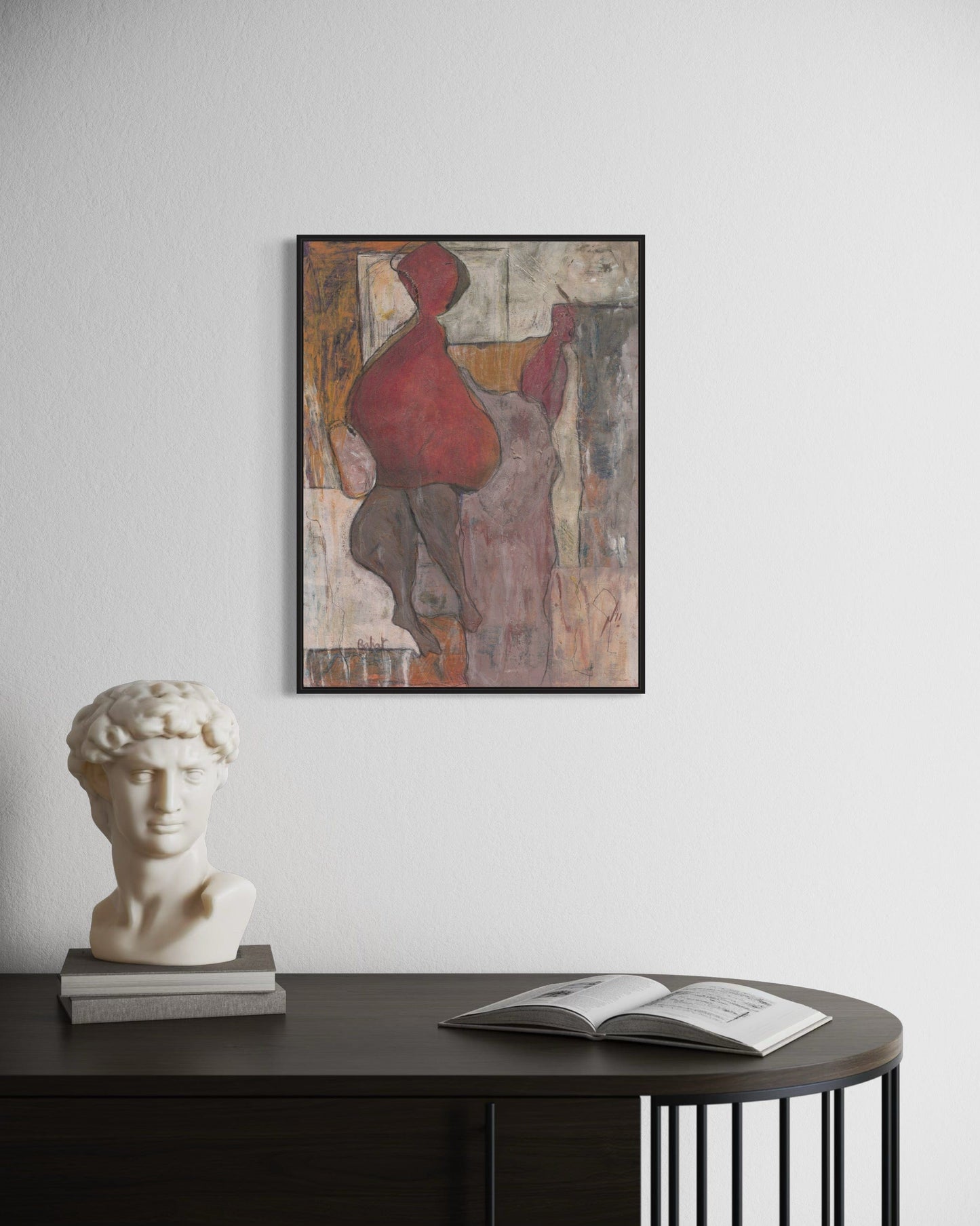 Framed abstract painting on a wall above a table with a bust and open book.