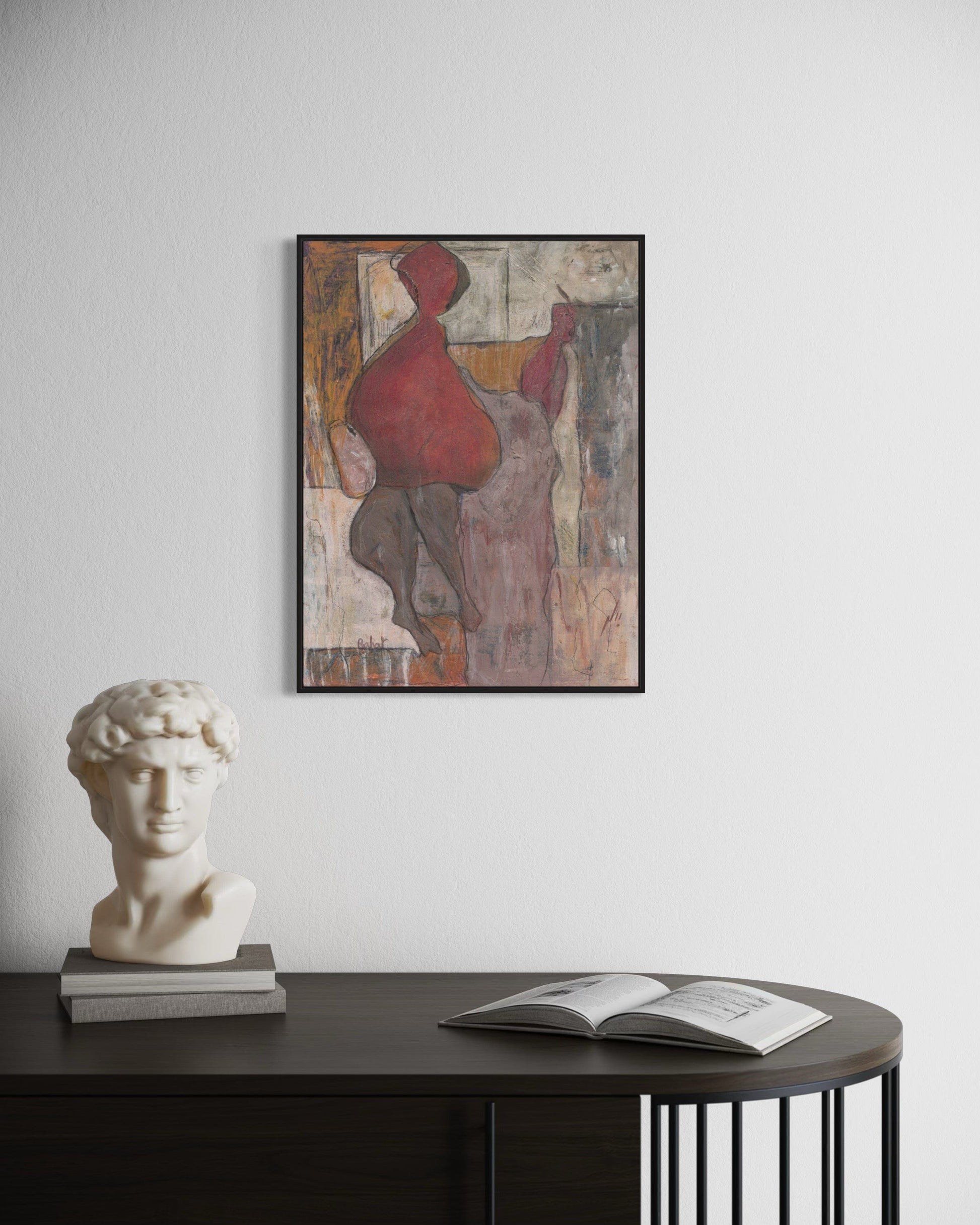 Framed abstract painting on a wall above a table with a bust and open book.