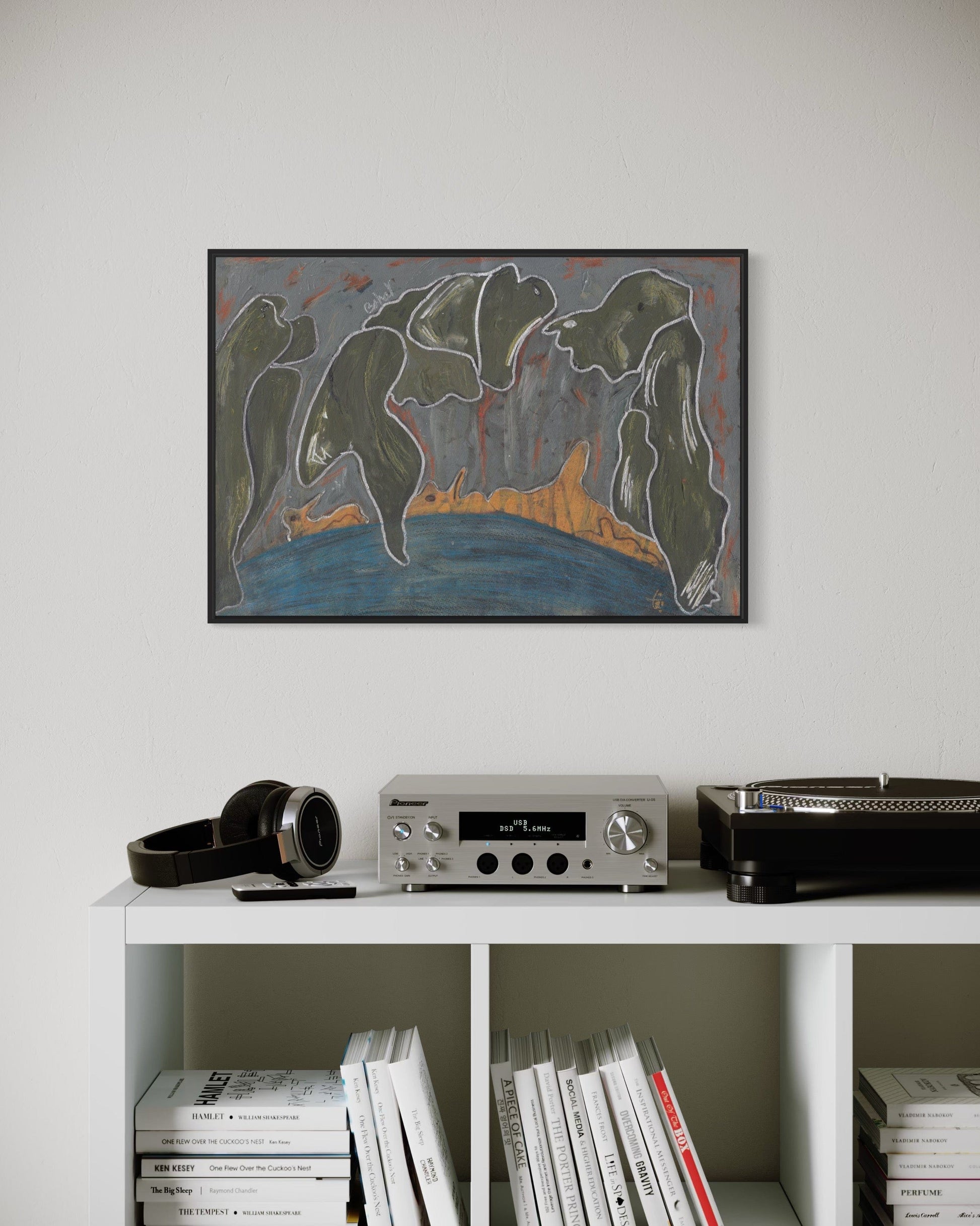 Framed abstract painting on a wall above a white shelf with electronic equipment and books.