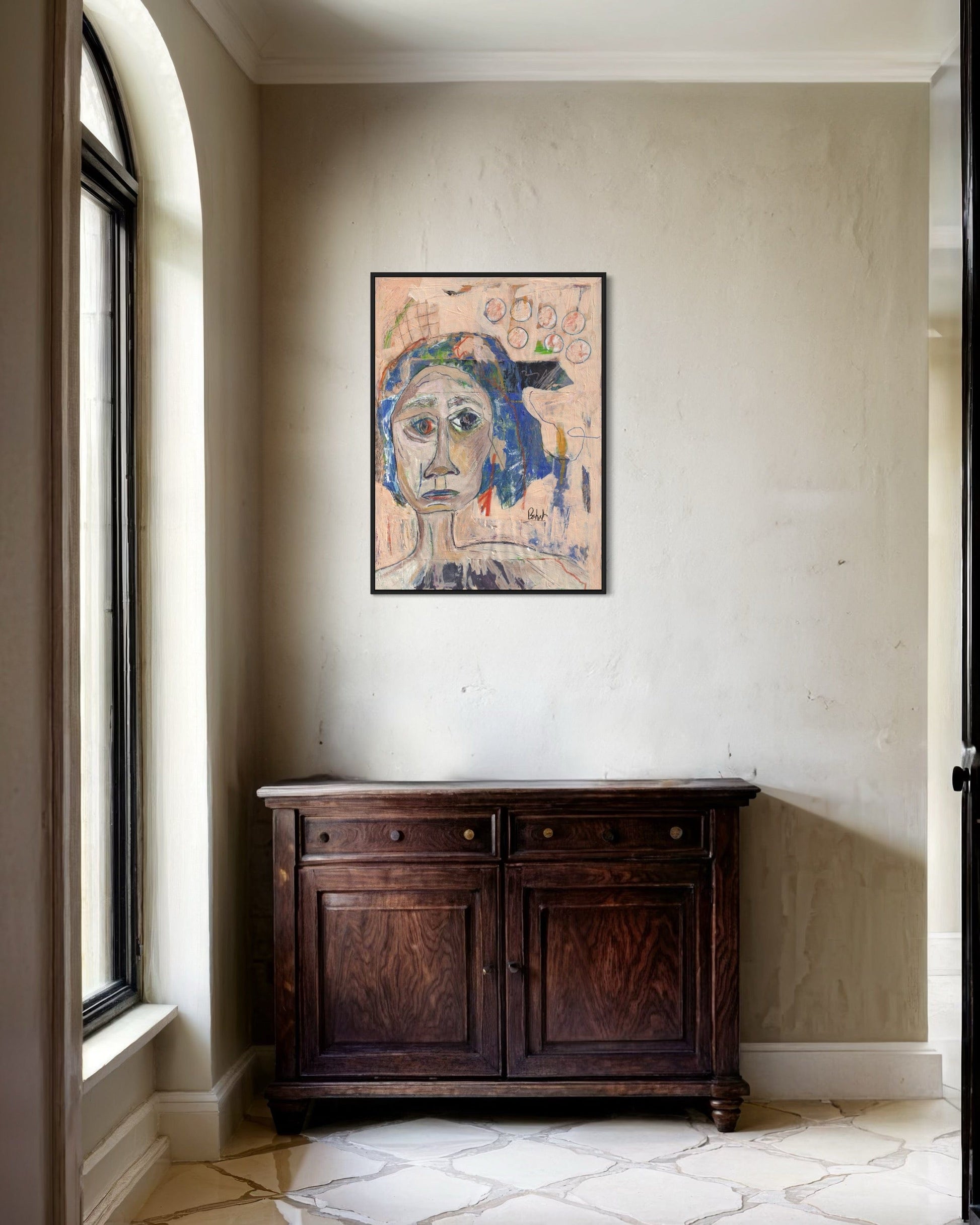 Artistic portrait on a wall above a wooden cabinet in a room with a window.
