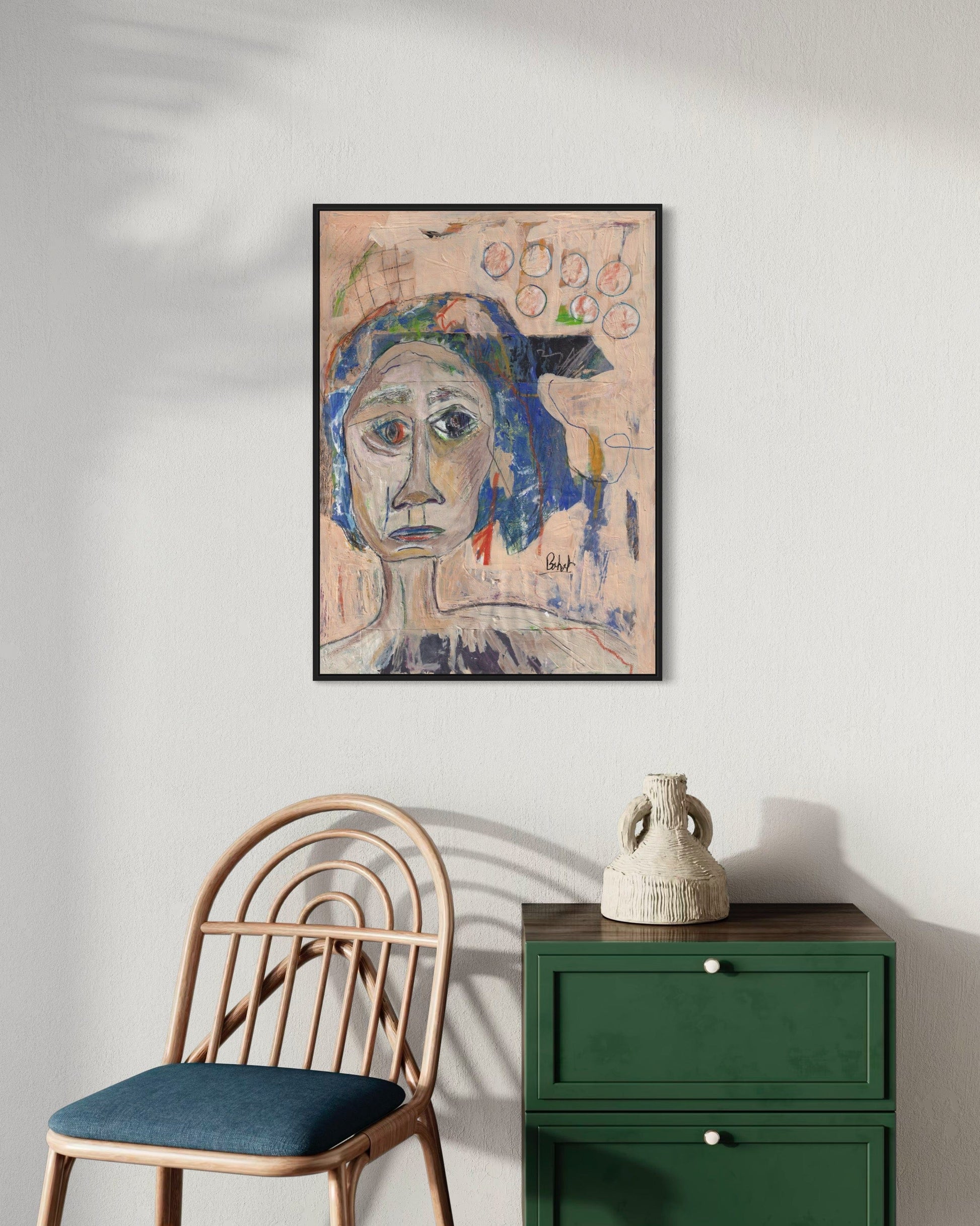 Framed abstract artwork on a wall above a green cabinet and wooden chair.