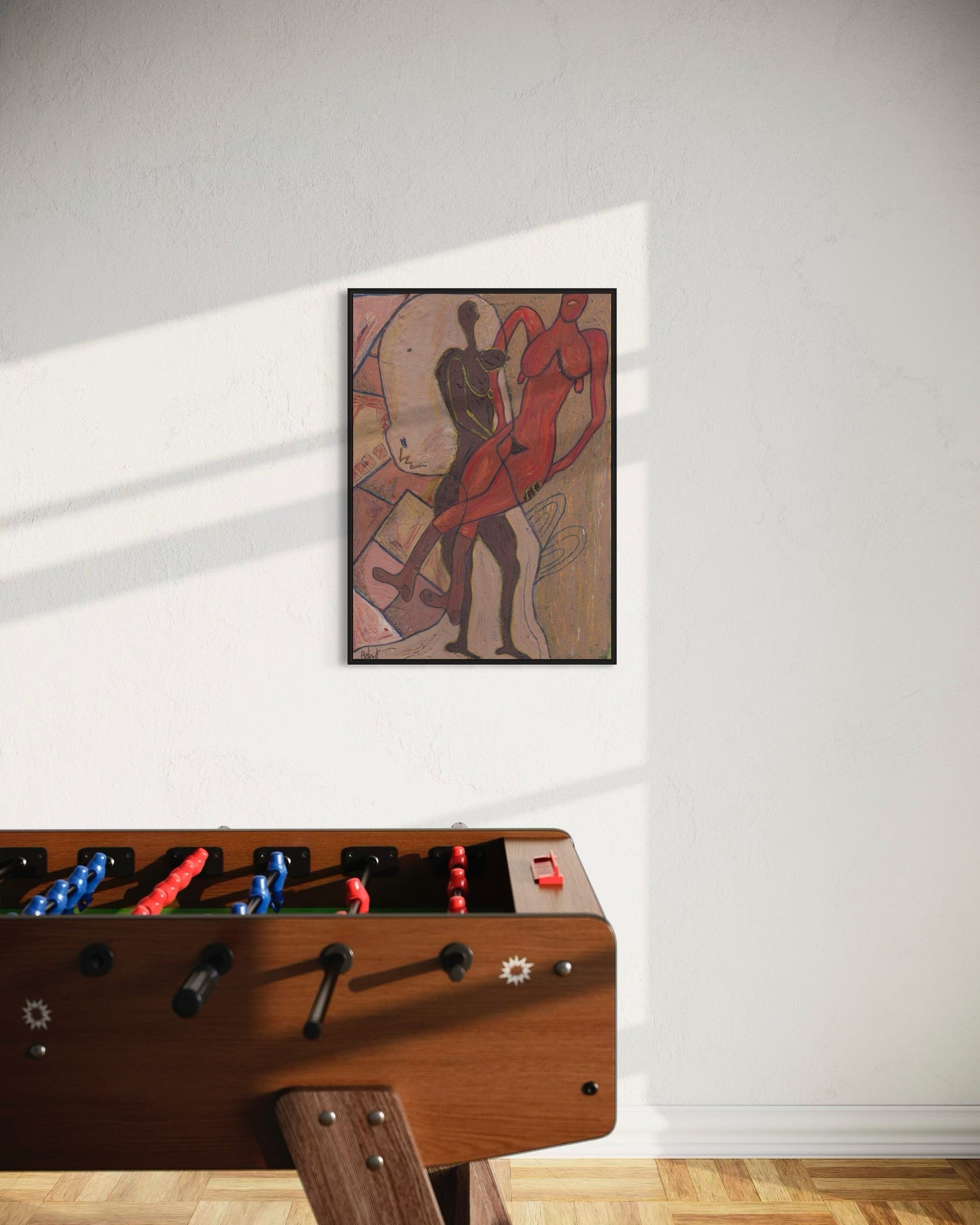 Wooden foosball table with a framed artwork on the wall above it.