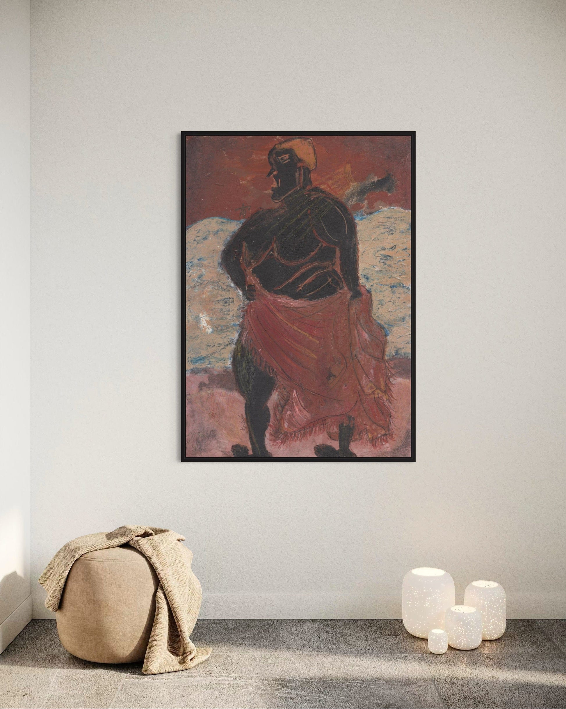 Framed artwork of a figure with a red garment on a white wall, with a beige pouf and white cylindrical objects on the floor.