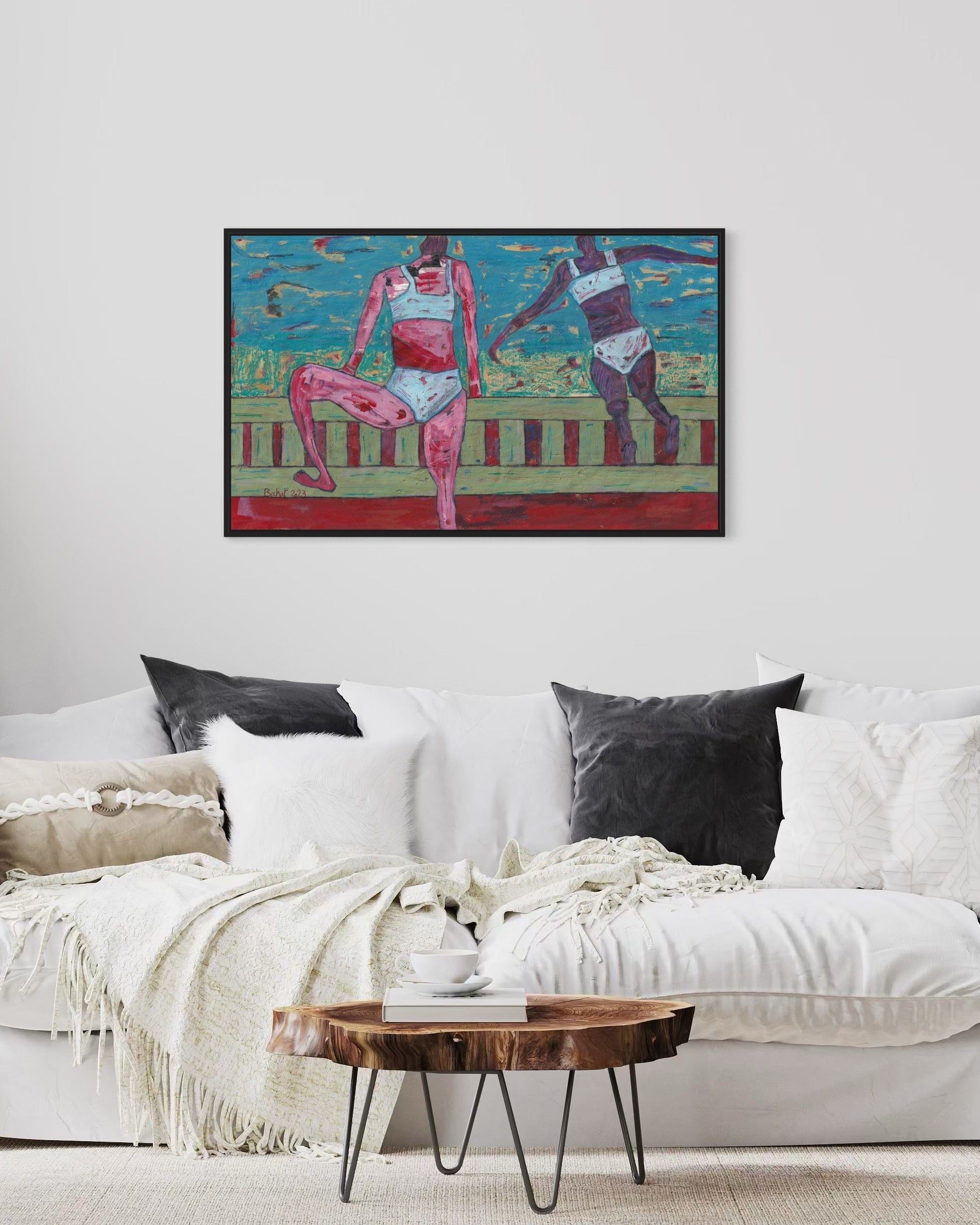 Framed artwork of two figures on a white wall above a white sofa with decorative pillows.