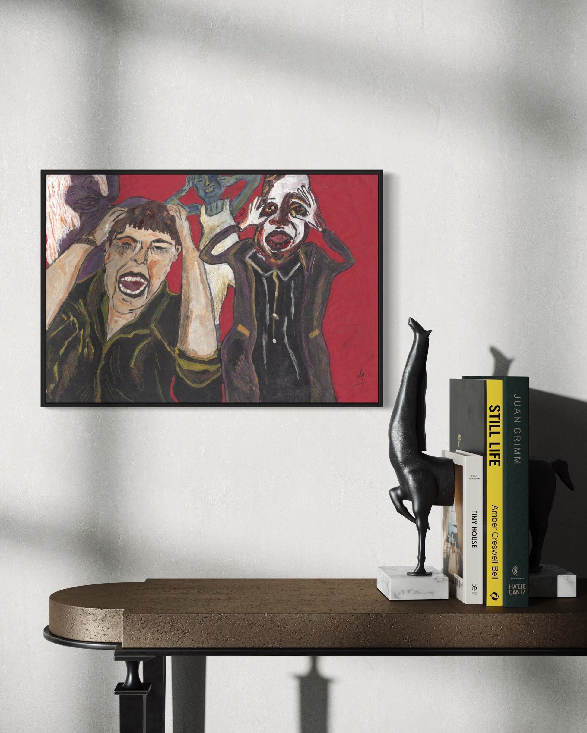 Framed artwork on a wall above a table with books and a sculpture.