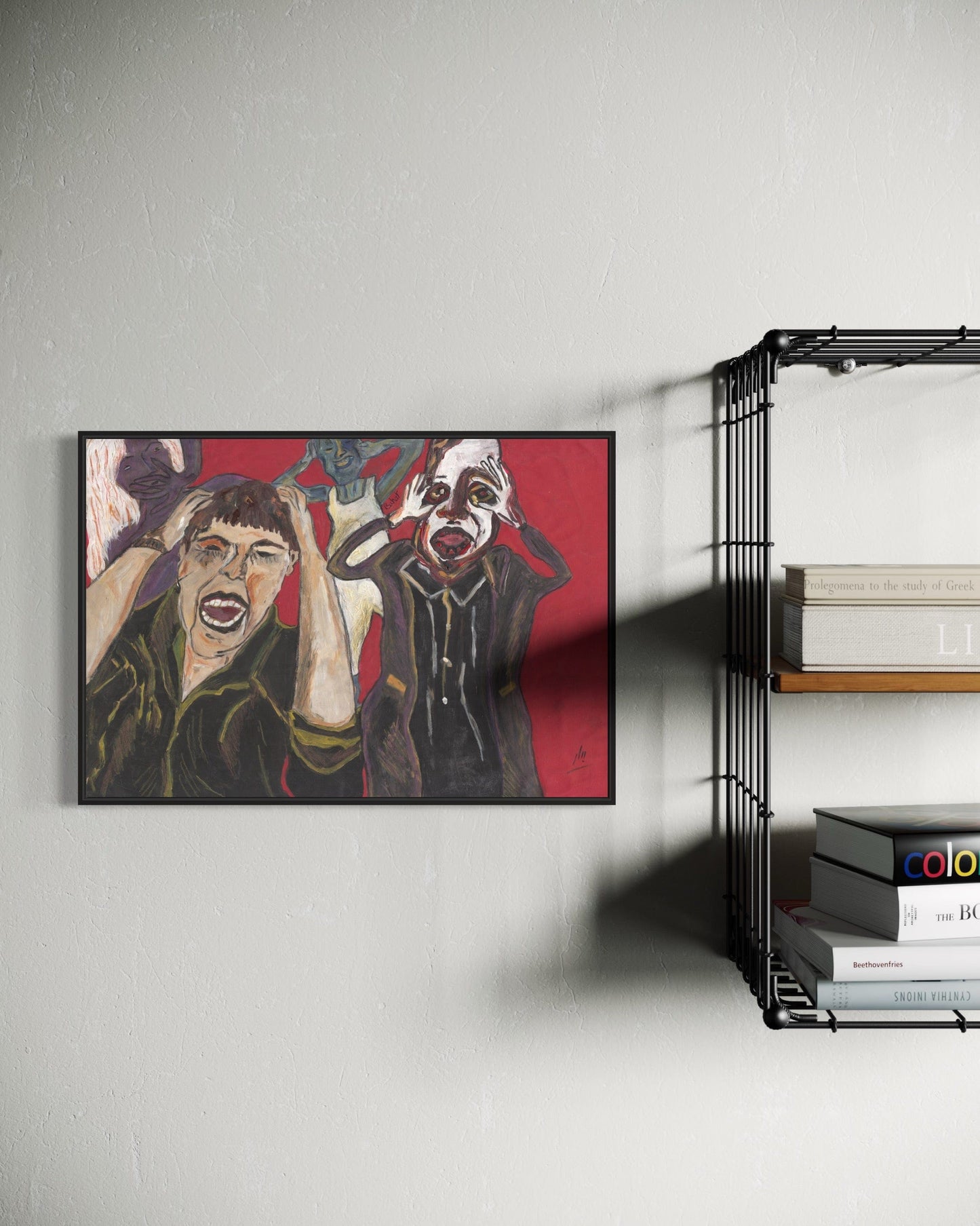Framed artwork of two figures on a red background hanging on a wall next to a bookshelf.