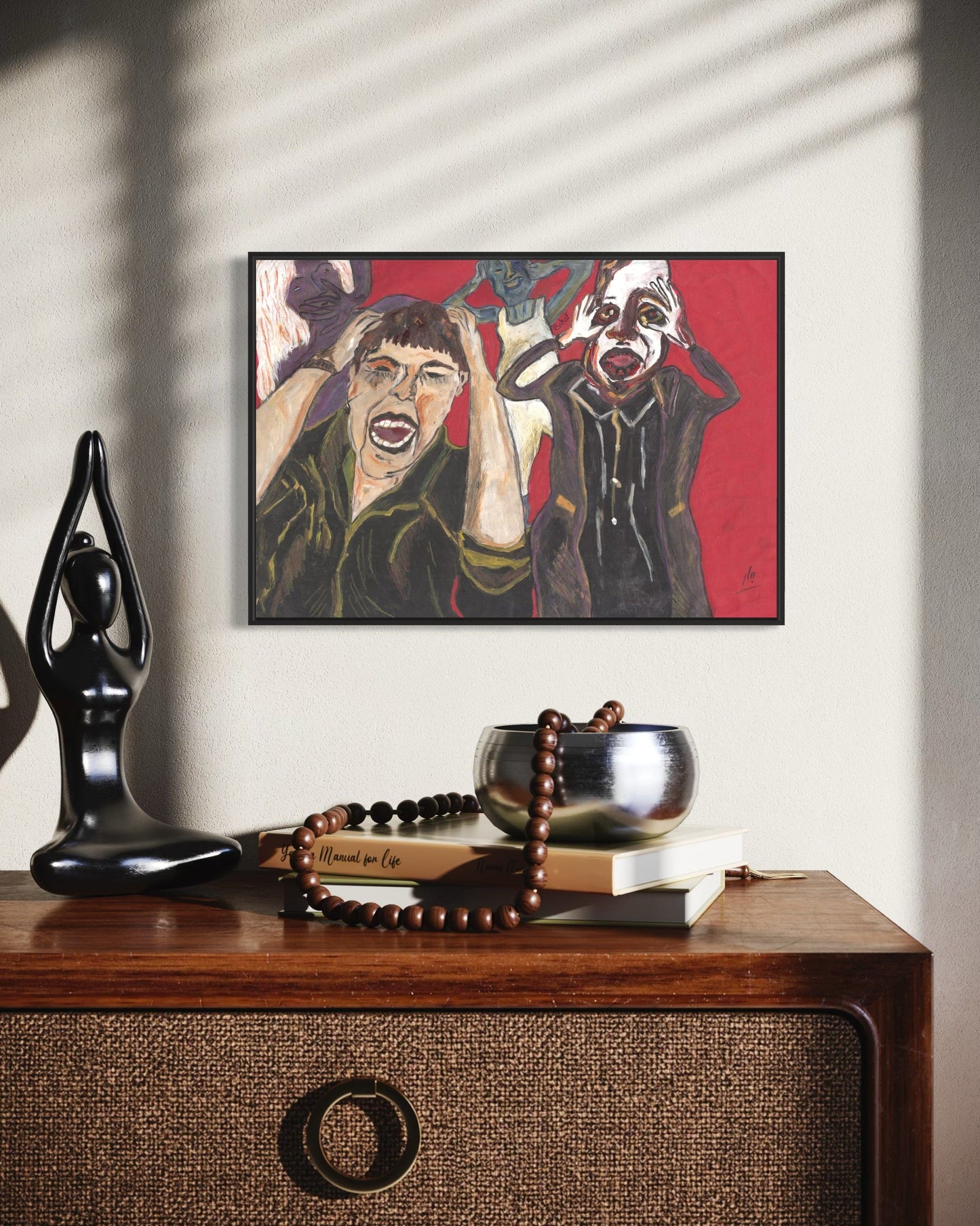 Framed artwork of two figures on a wall above a wooden surface with decorative items.