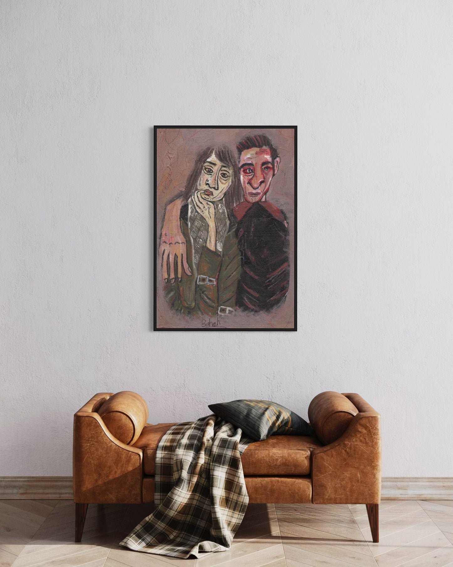 Framed artwork of two people on a wall above a brown sofa with a plaid blanket.
