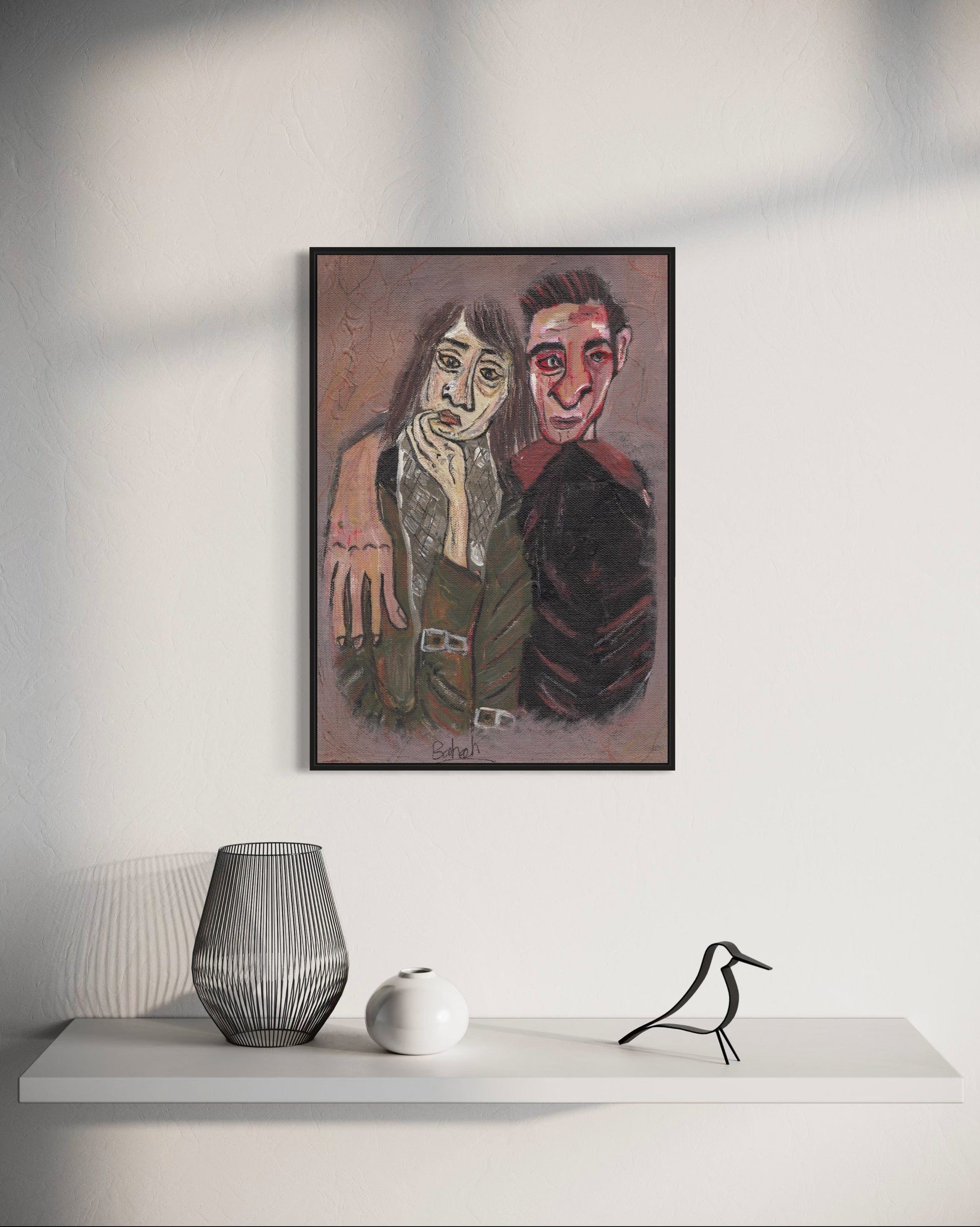 Framed artwork of two people on a white wall above a shelf with decorative items.