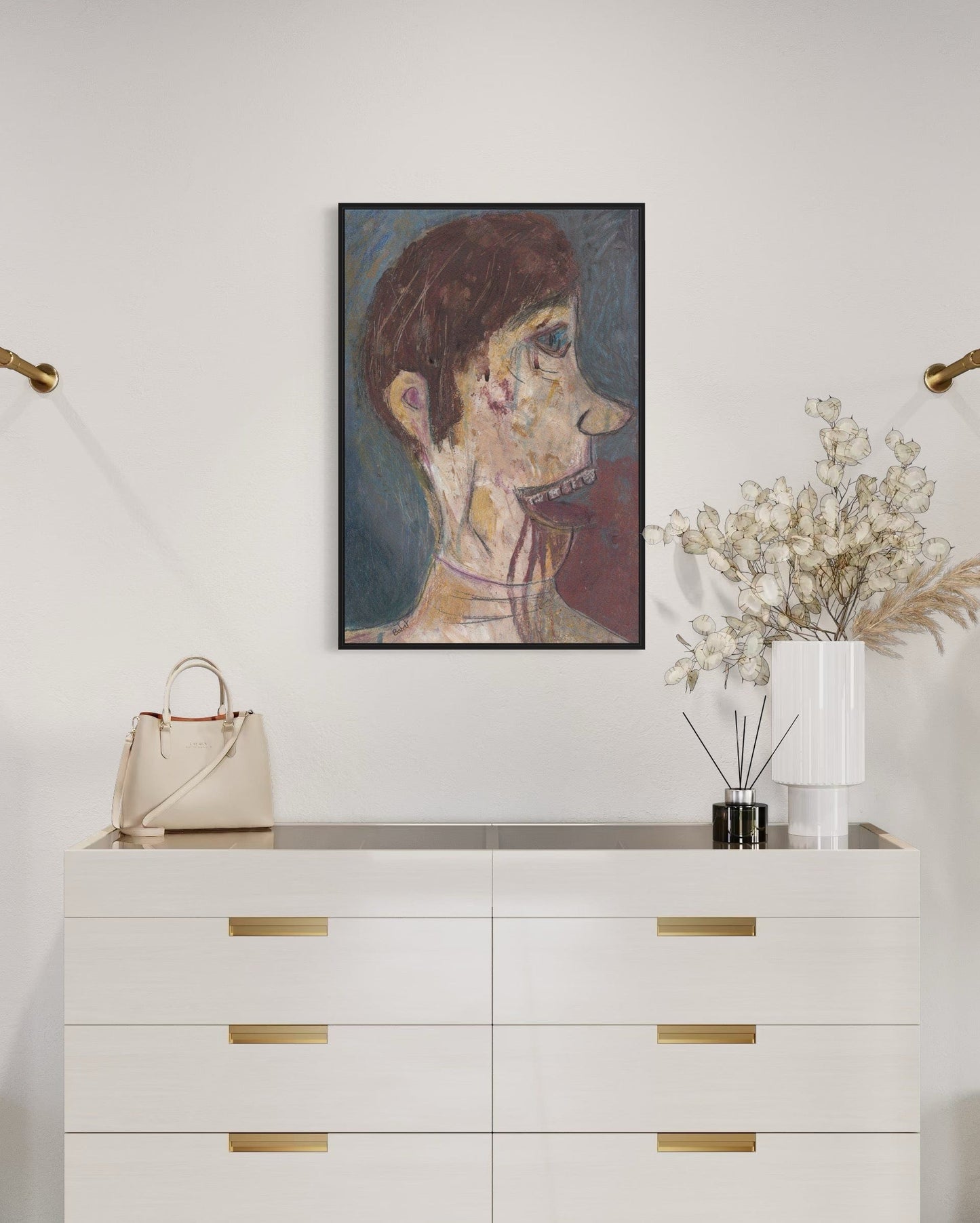 White dresser with gold handles, beige handbag, framed artwork, and decorative plants on a white wall.