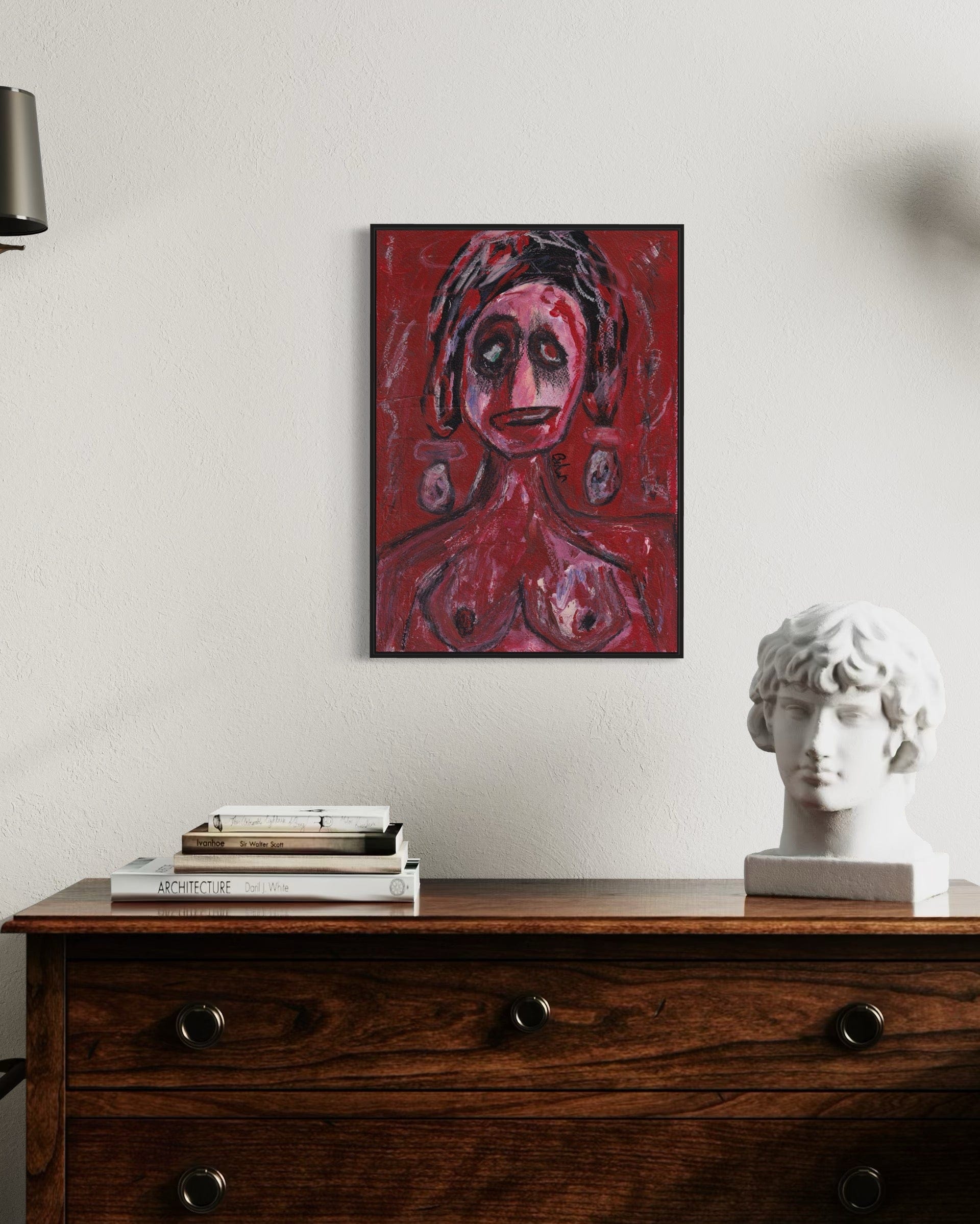 Artistic portrait on a wall above a wooden dresser with books and a sculpture.