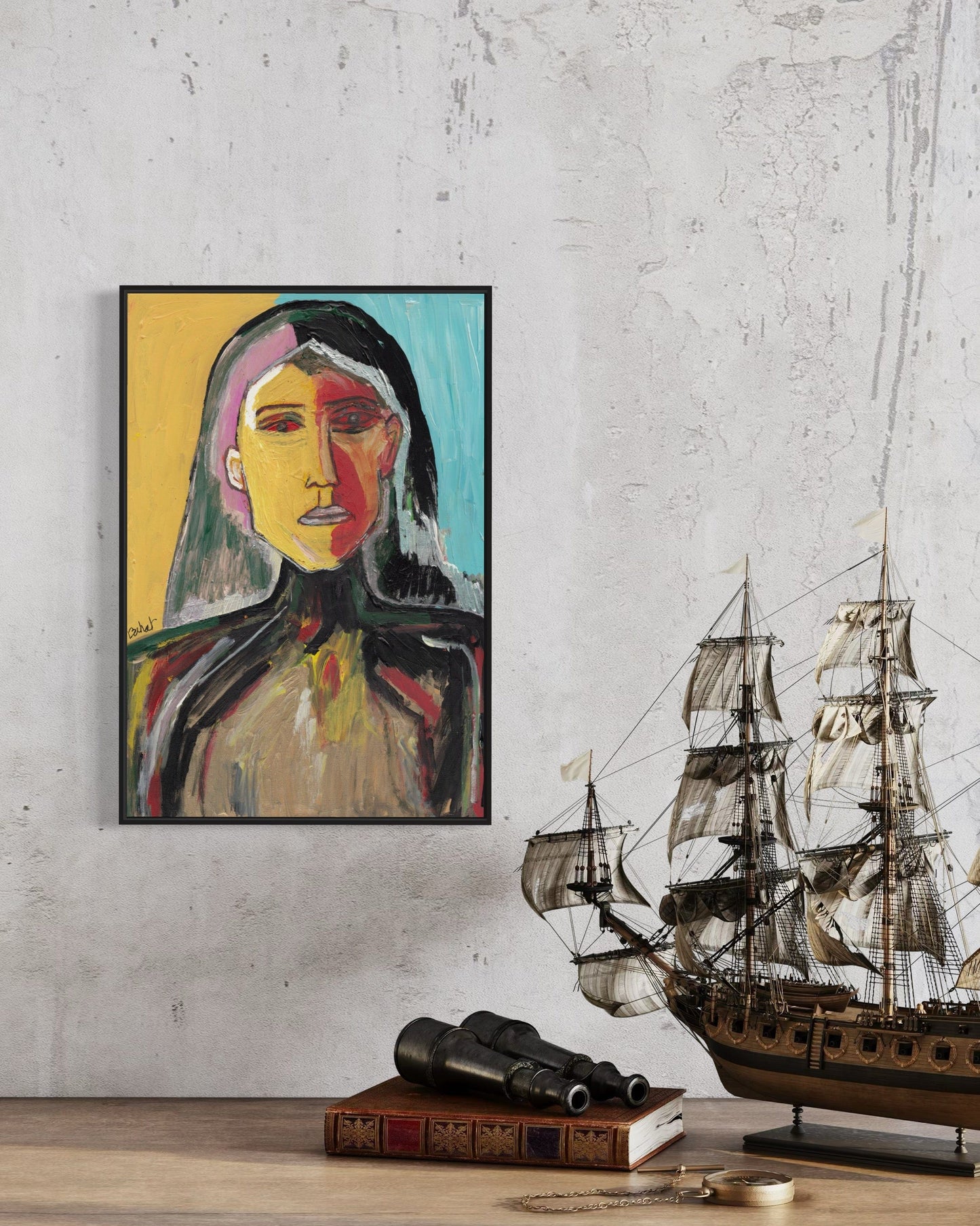 Framed abstract portrait on a wall with a model ship and books below.