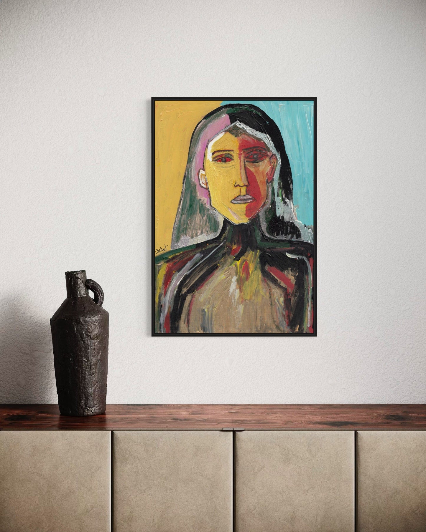 Framed abstract portrait on a wall above a wooden shelf with a vase.