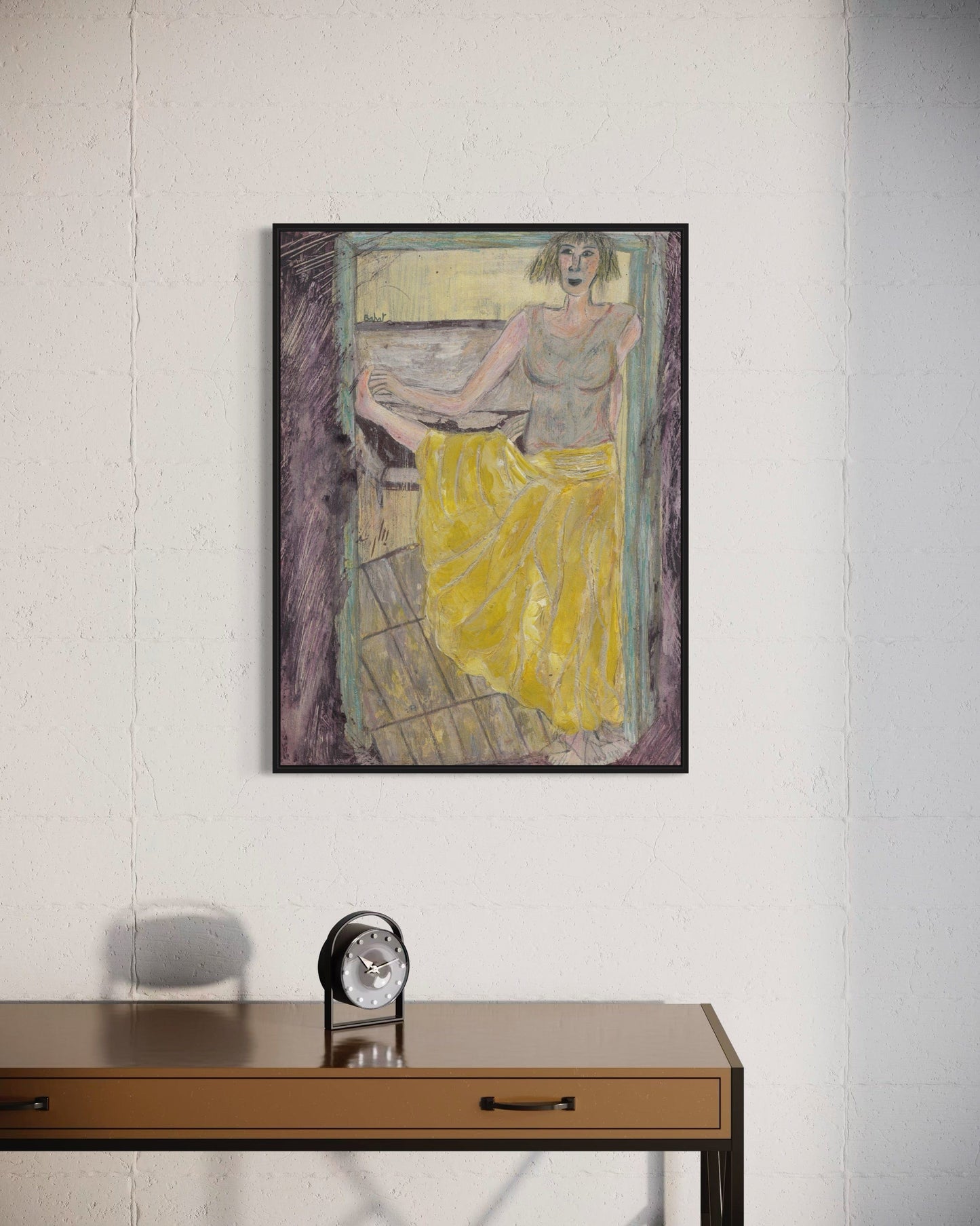 Framed painting of a woman in a yellow dress on a white wall above a wooden desk with a clock.