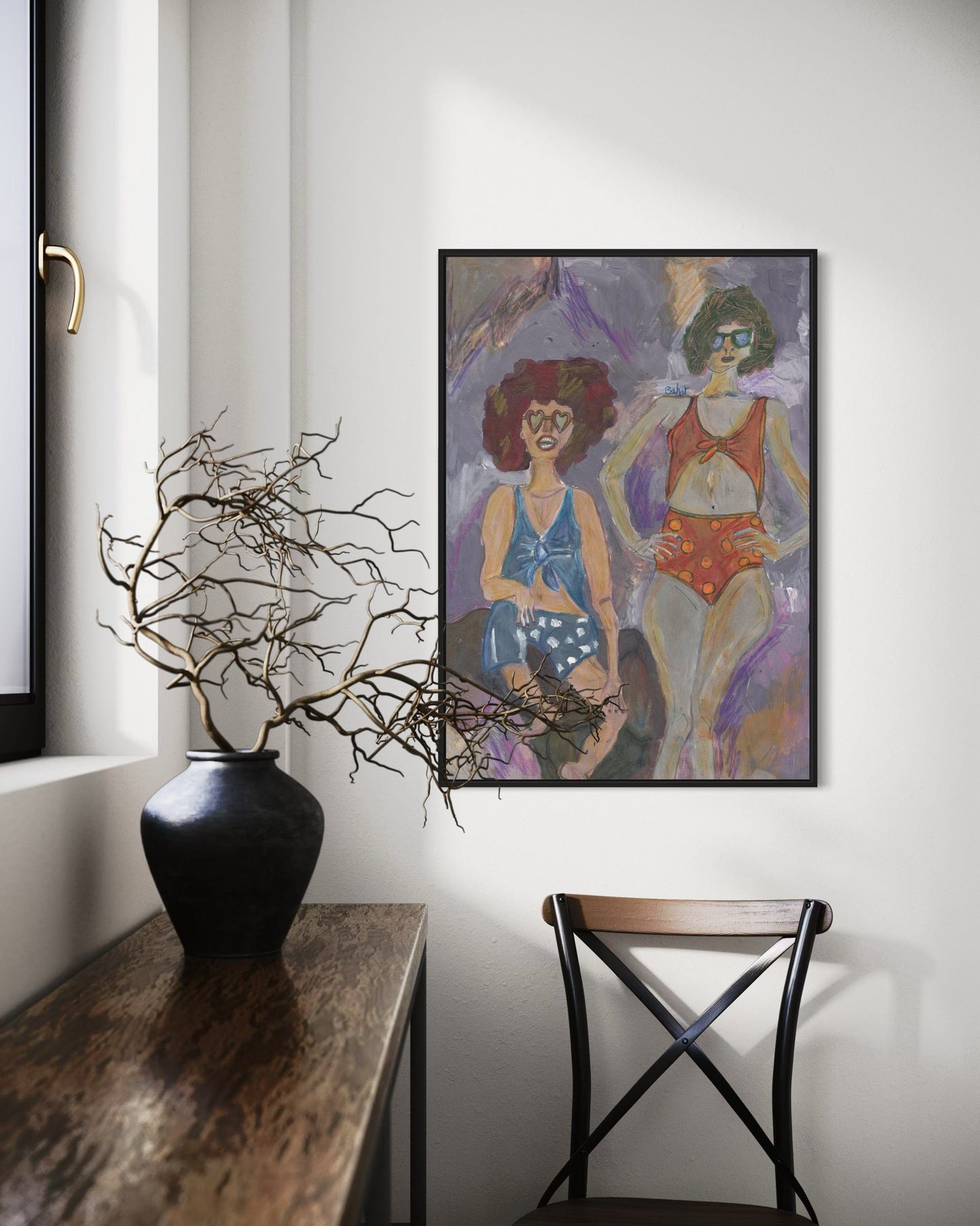 Framed artwork of two women on a wall above a vase with branches.