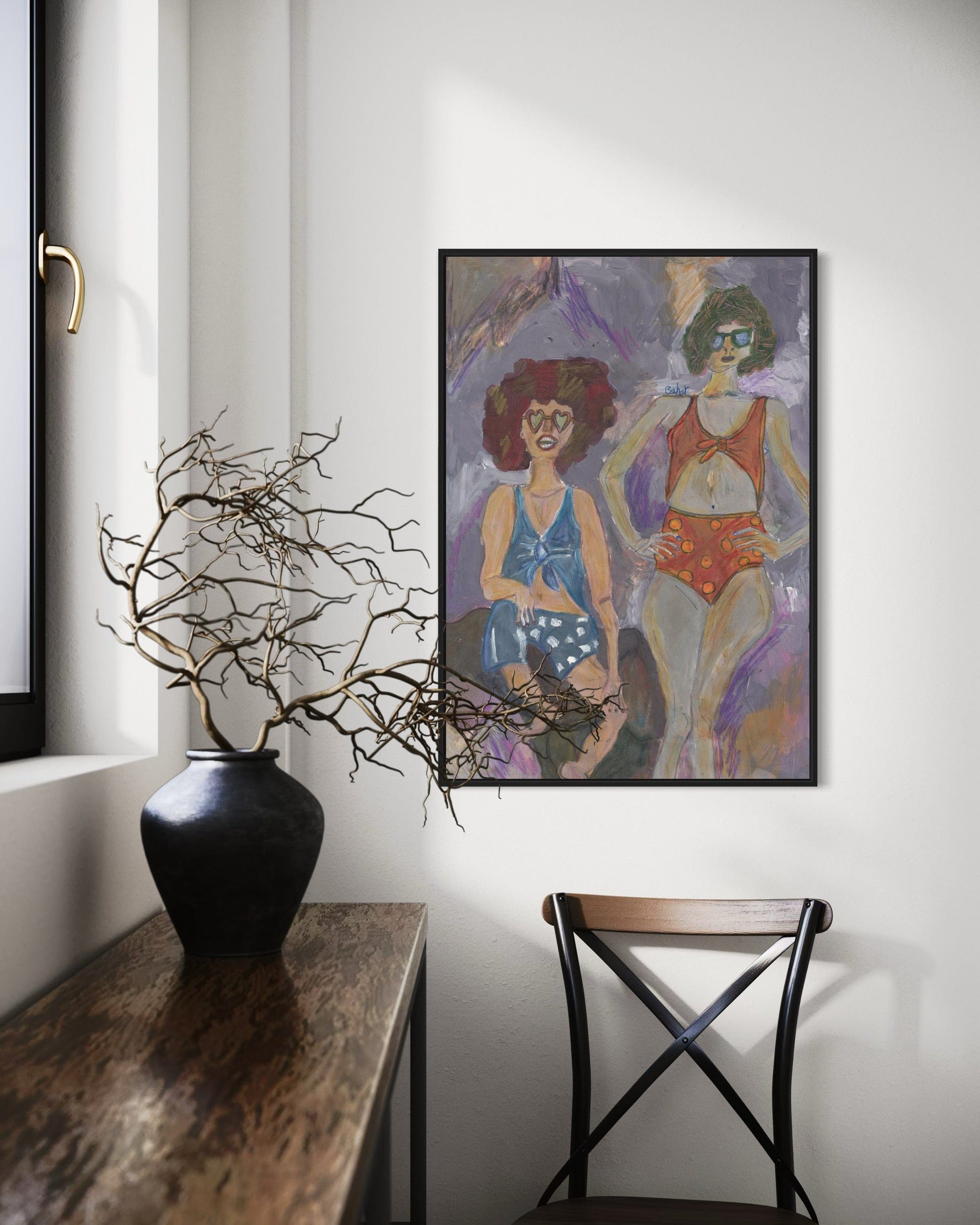 Framed artwork of two women on a wall above a vase with branches.