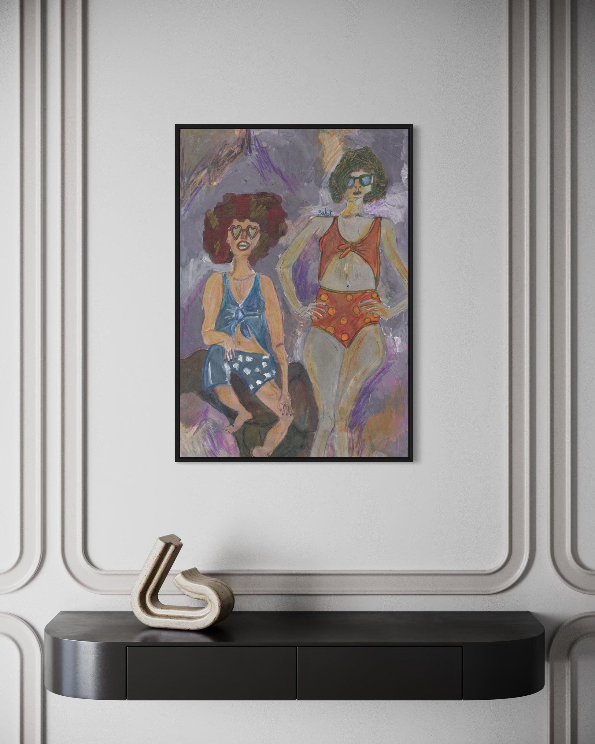 Framed artwork of two women in swimsuits on a wall above a black console table.