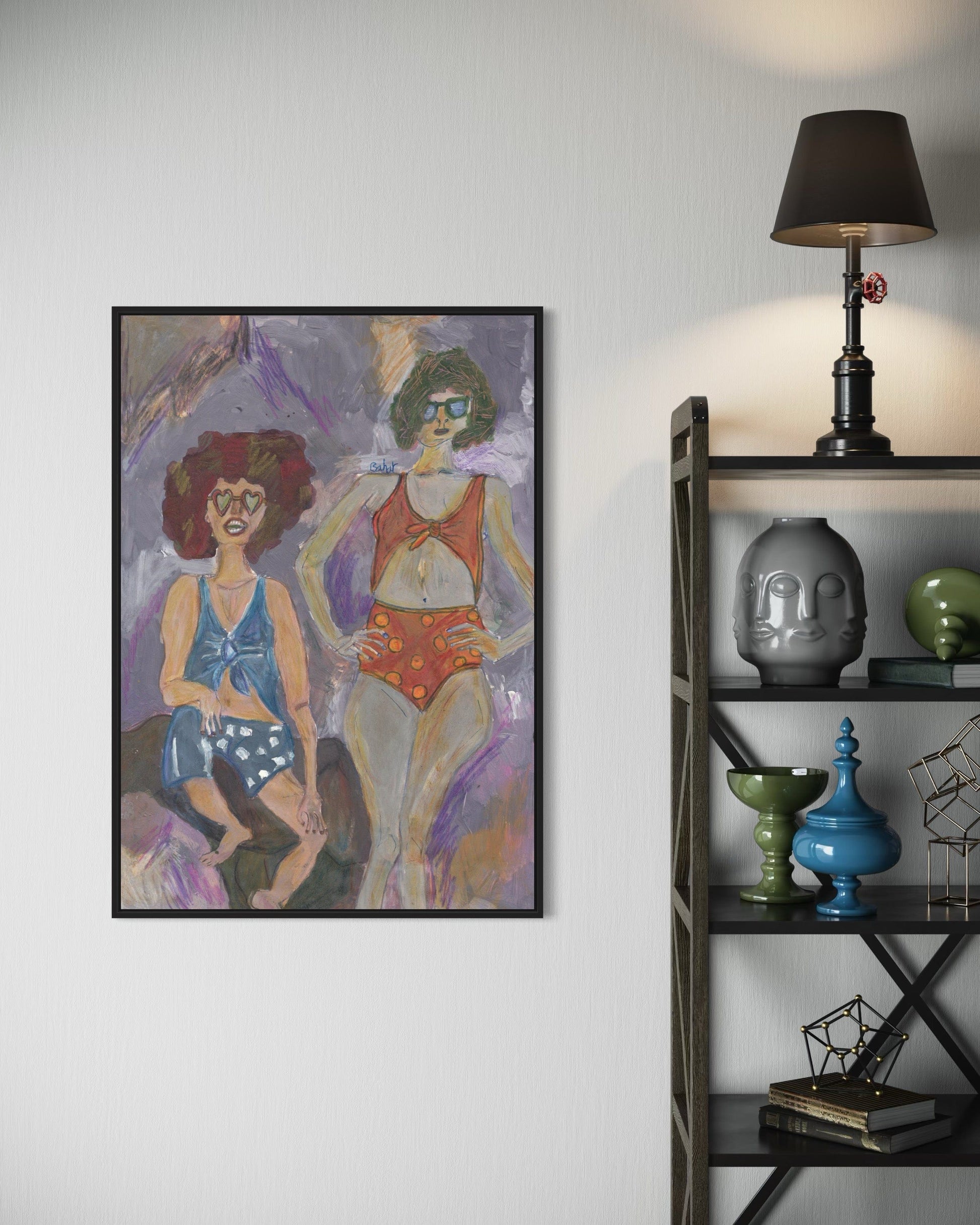 Framed artwork of two women in swimsuits on a wall next to a shelf with decorative items.