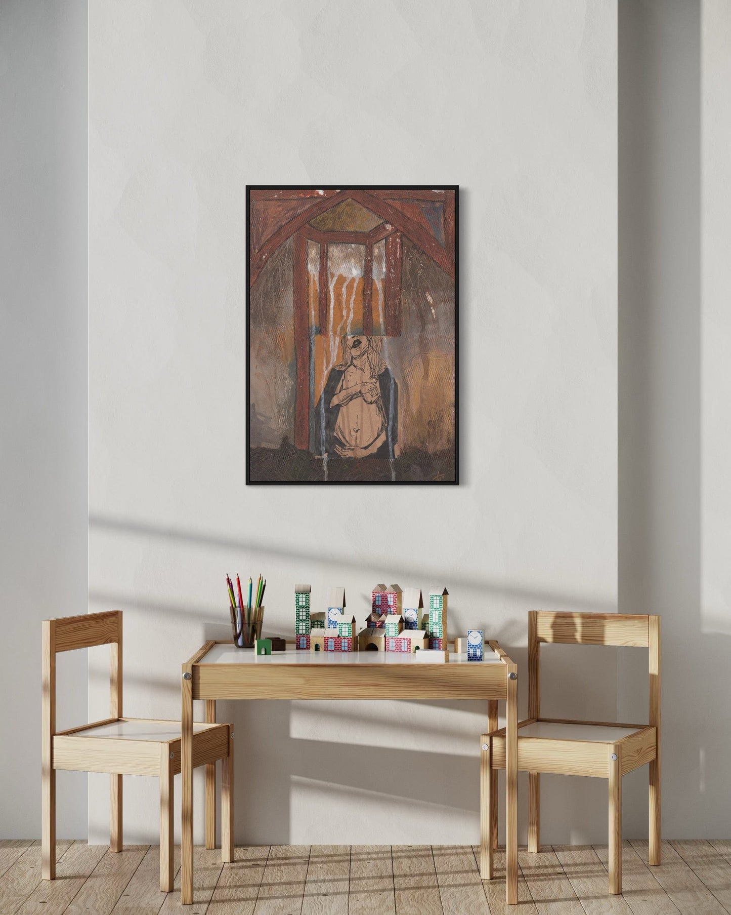 Small wooden table with chairs and art supplies against a plain wall with a framed painting.