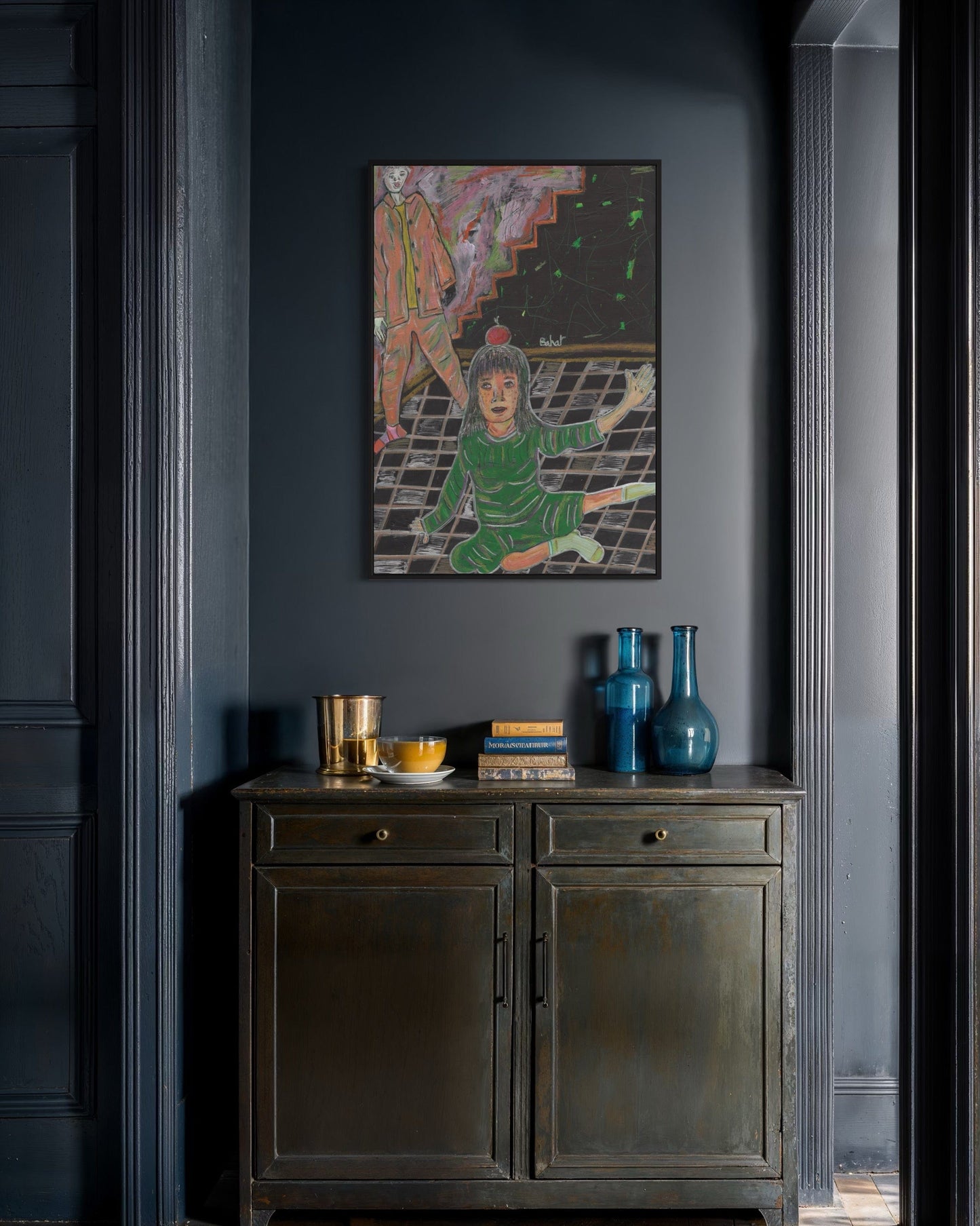 Framed artwork on a dark wall above a wooden cabinet with decorative items.
