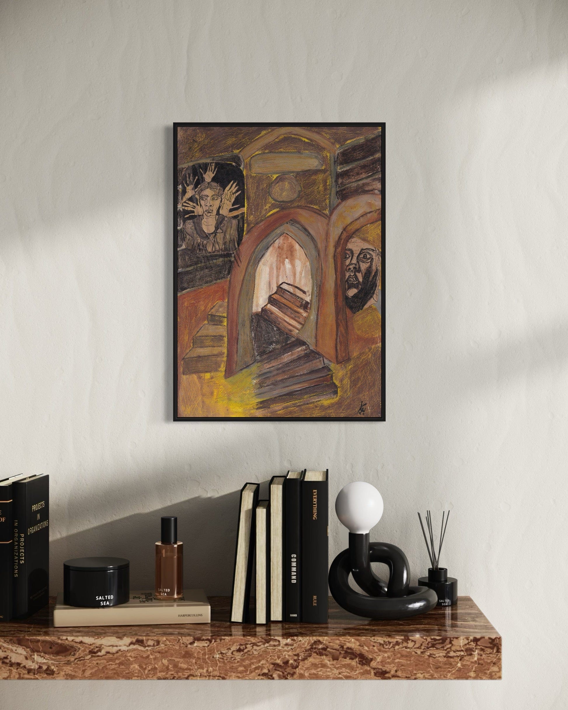 Framed artwork on a wall above a wooden shelf with books and decorative items.