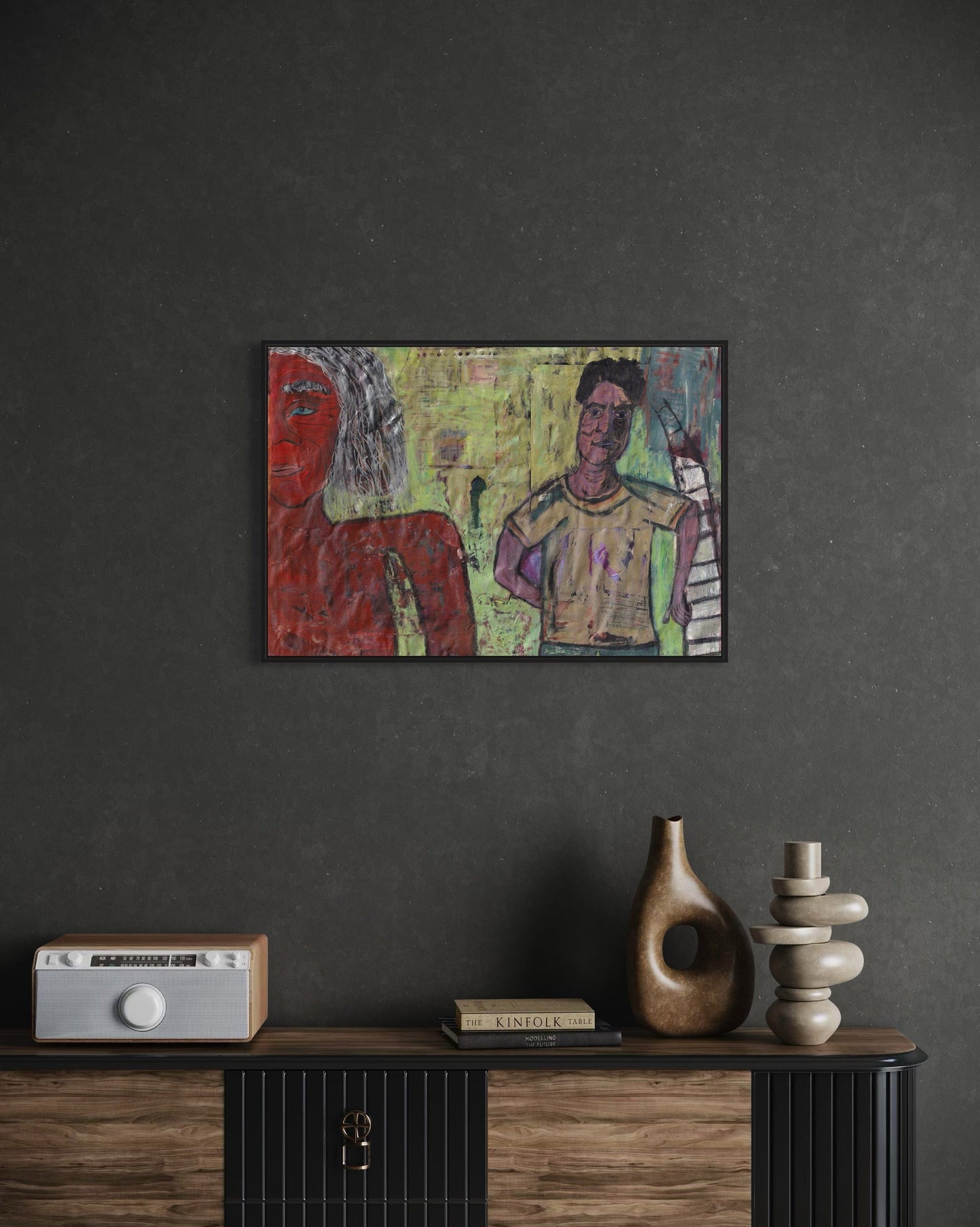 Abstract painting of two figures on a dark wall above a wooden cabinet with decorative items.