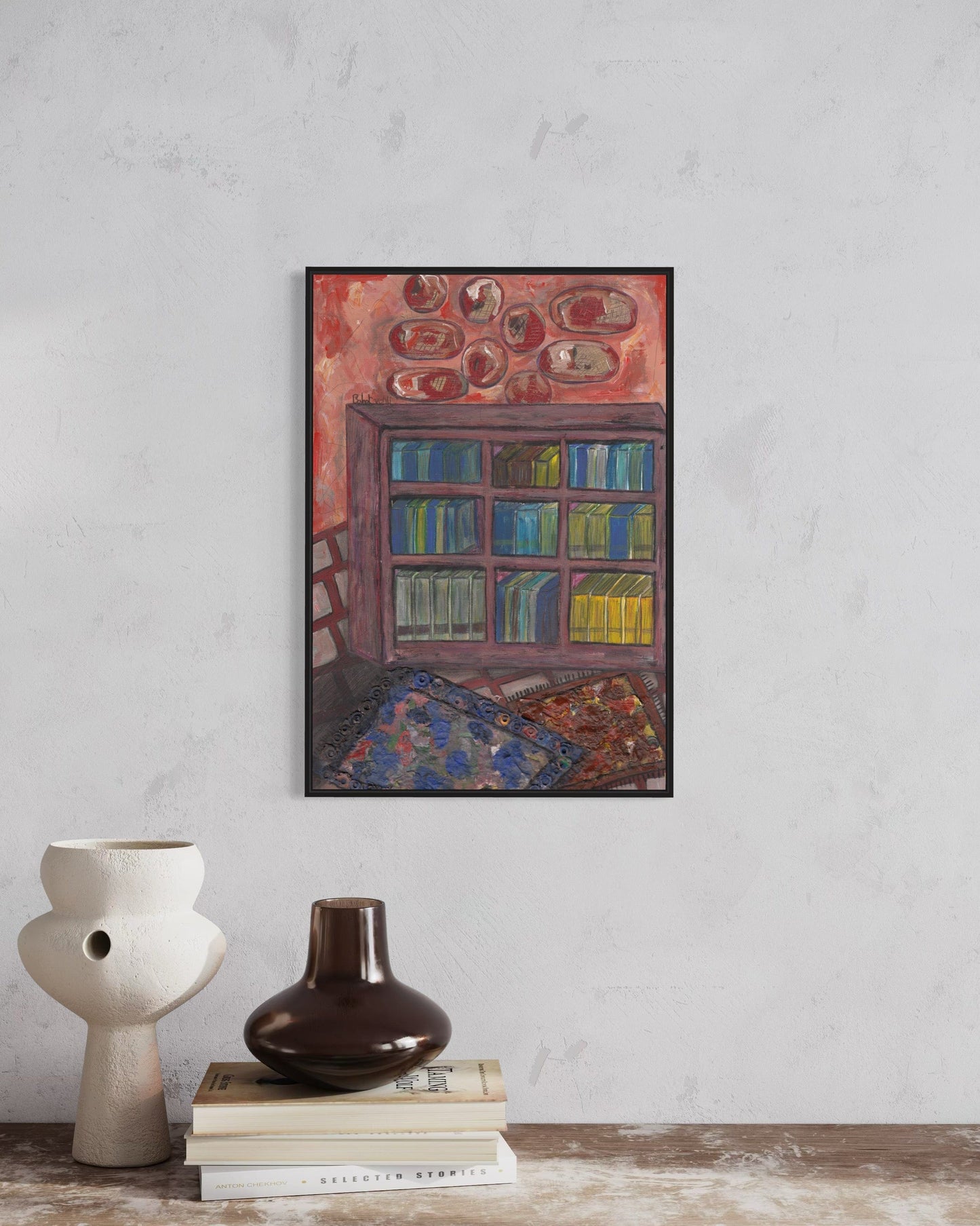 Framed artwork on a wall with two vases and books below.