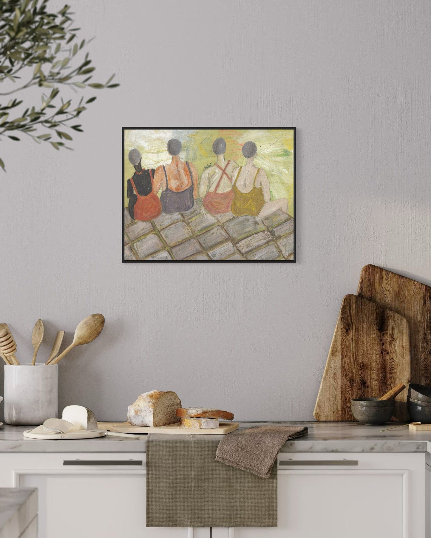 Framed artwork of three figures on a wall above a kitchen counter with various items.