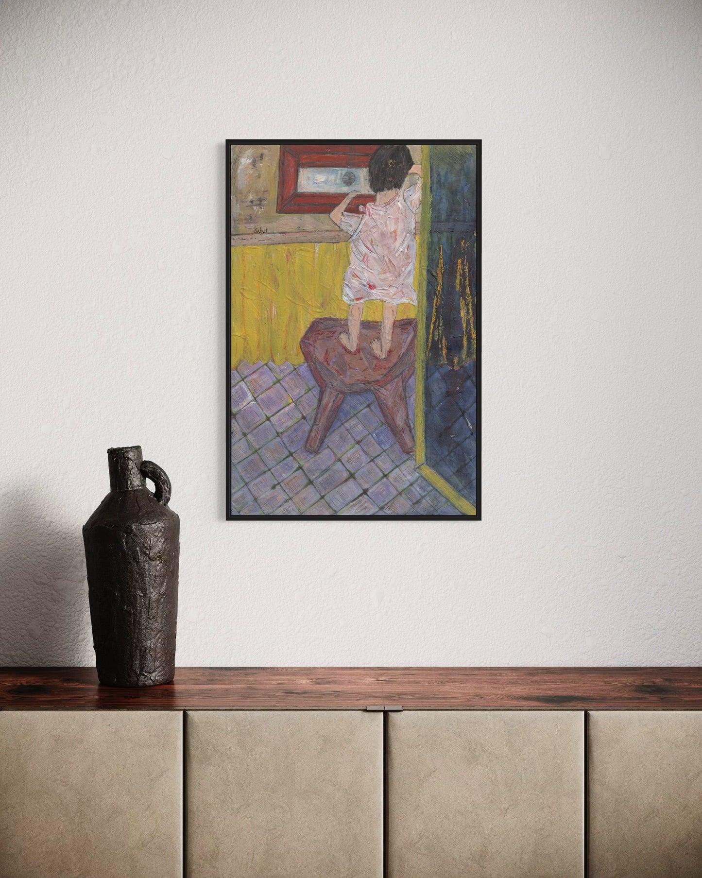 Framed artwork on a wall above a wooden shelf with a decorative vase.