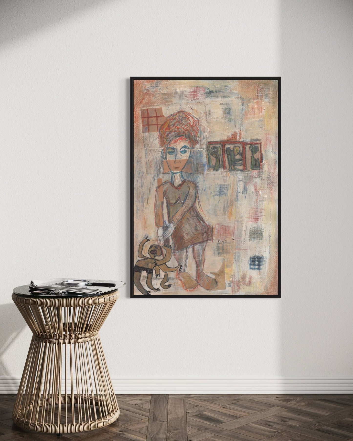 Framed artwork of a stylized figure on a wall above a wicker side table.