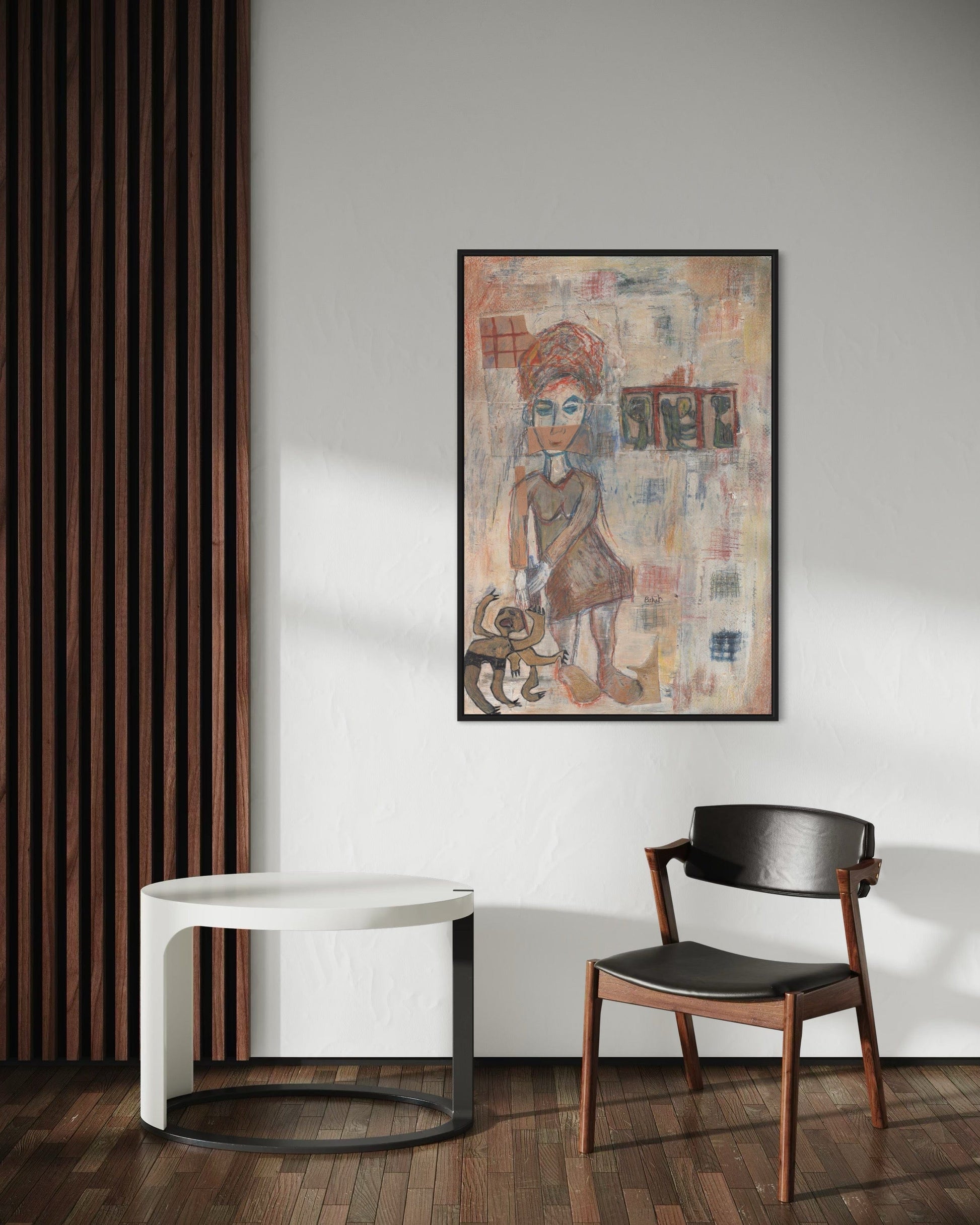 Framed artwork on a wall above a white table and black chair in a room with wooden flooring.
