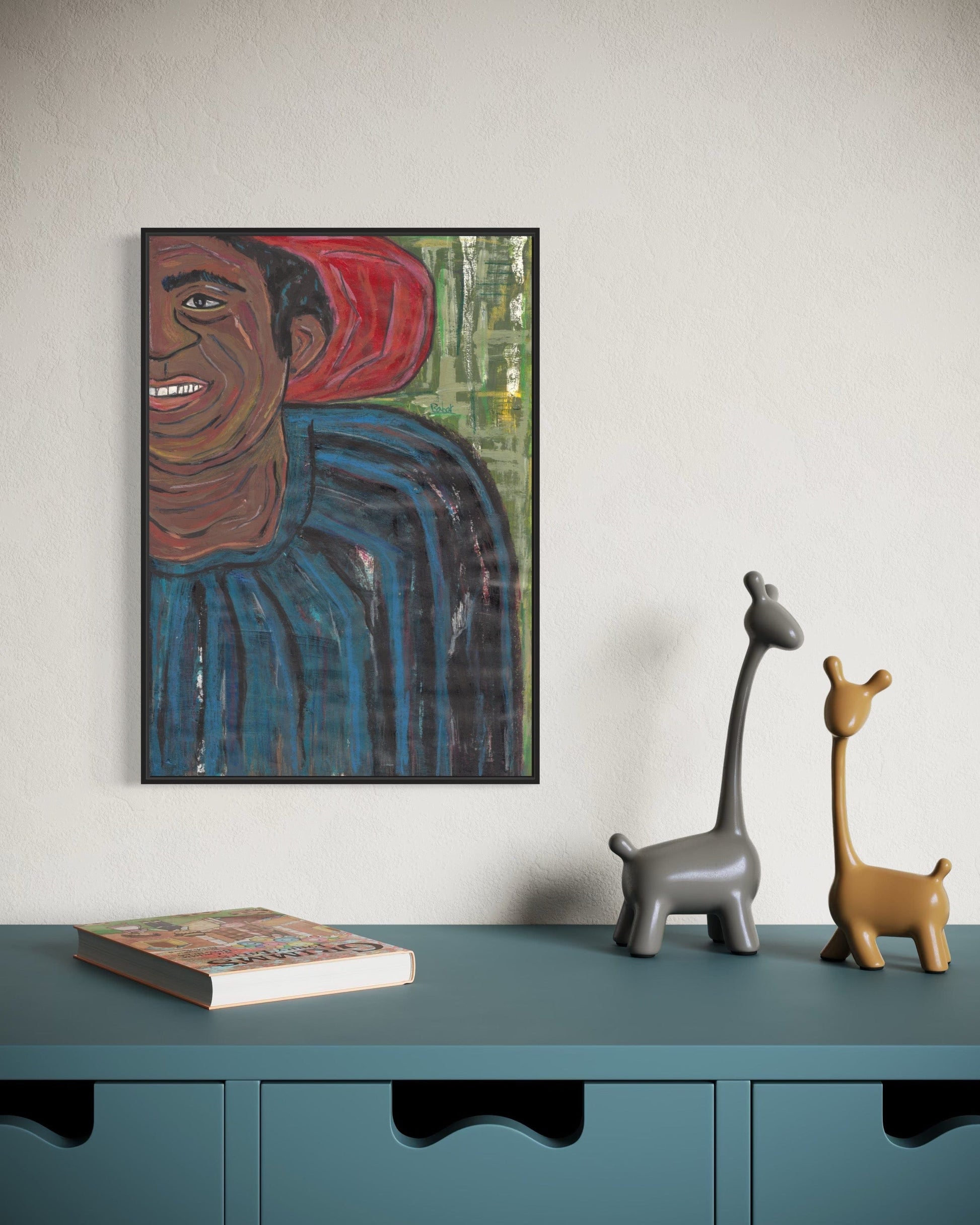 Framed artwork on a wall above a teal cabinet with decorative giraffes and a book.