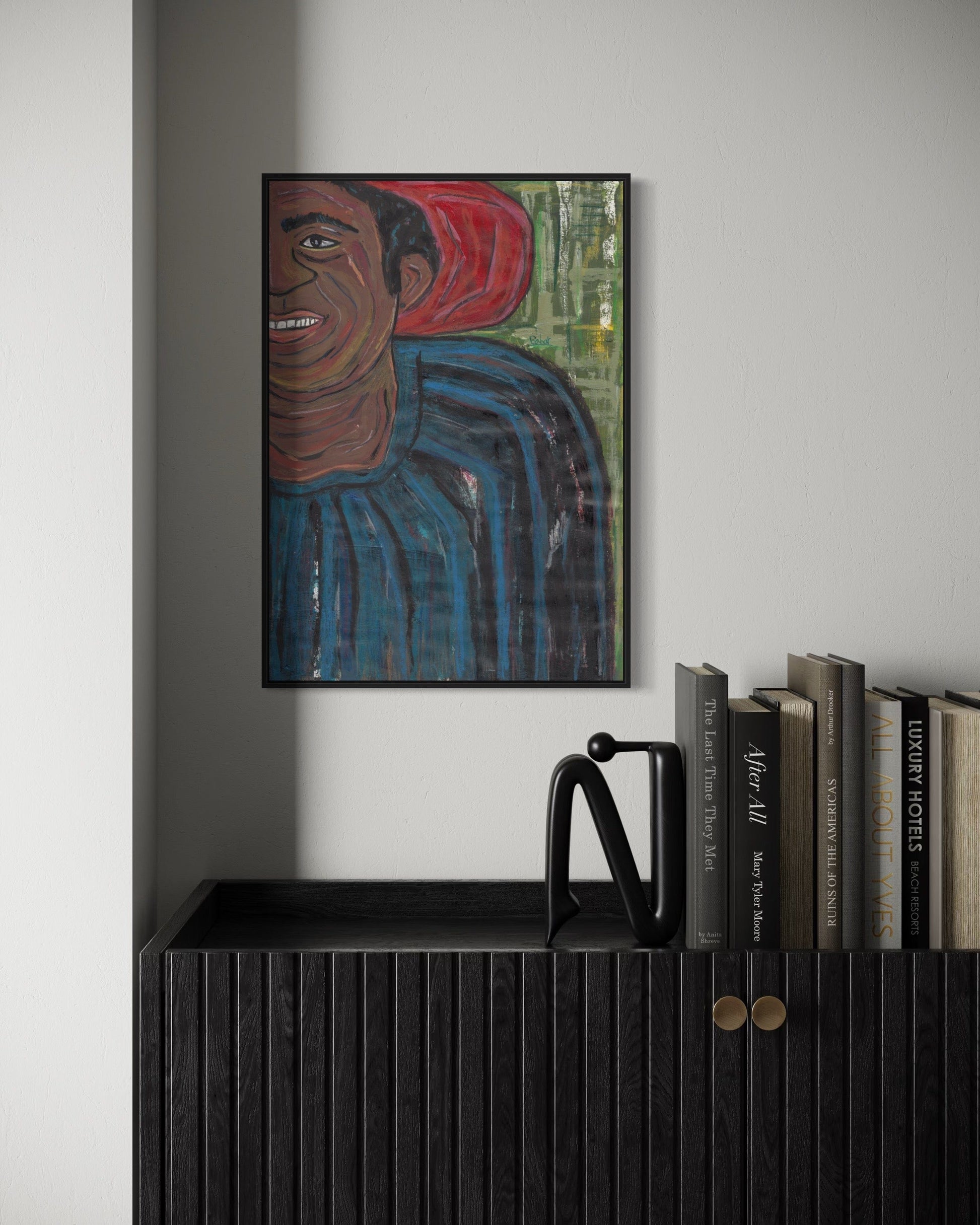 Framed artwork of a person with a red headscarf on a wall above a black cabinet with books.
