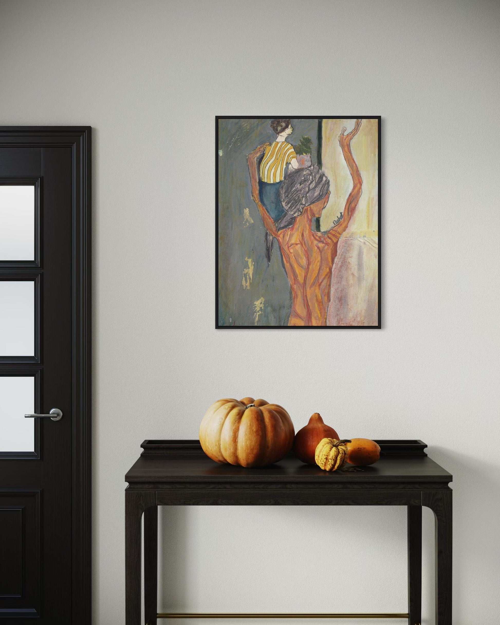 Framed artwork on a wall above a dark wooden table with pumpkins.