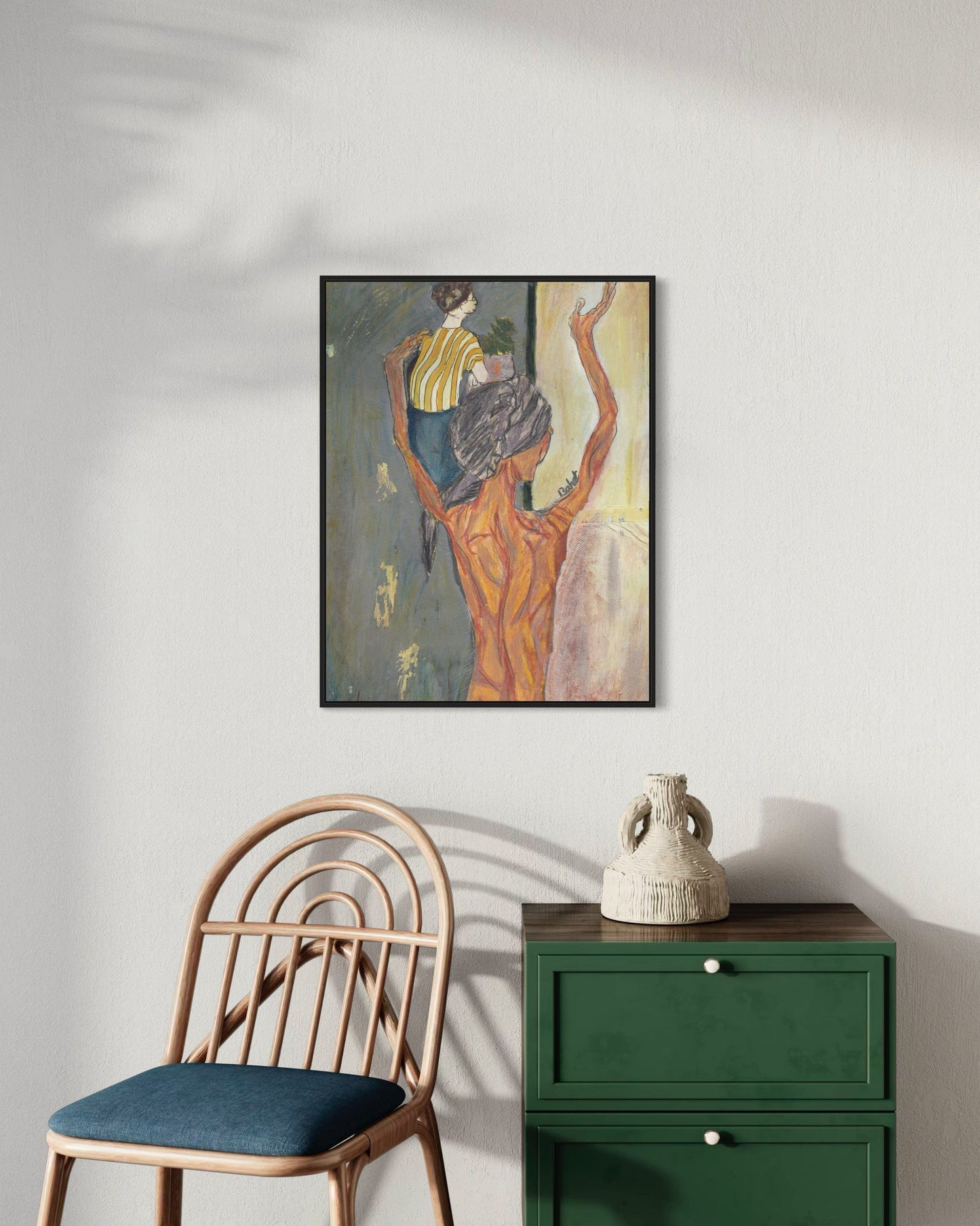 Framed artwork on a wall above a green cabinet and chair.