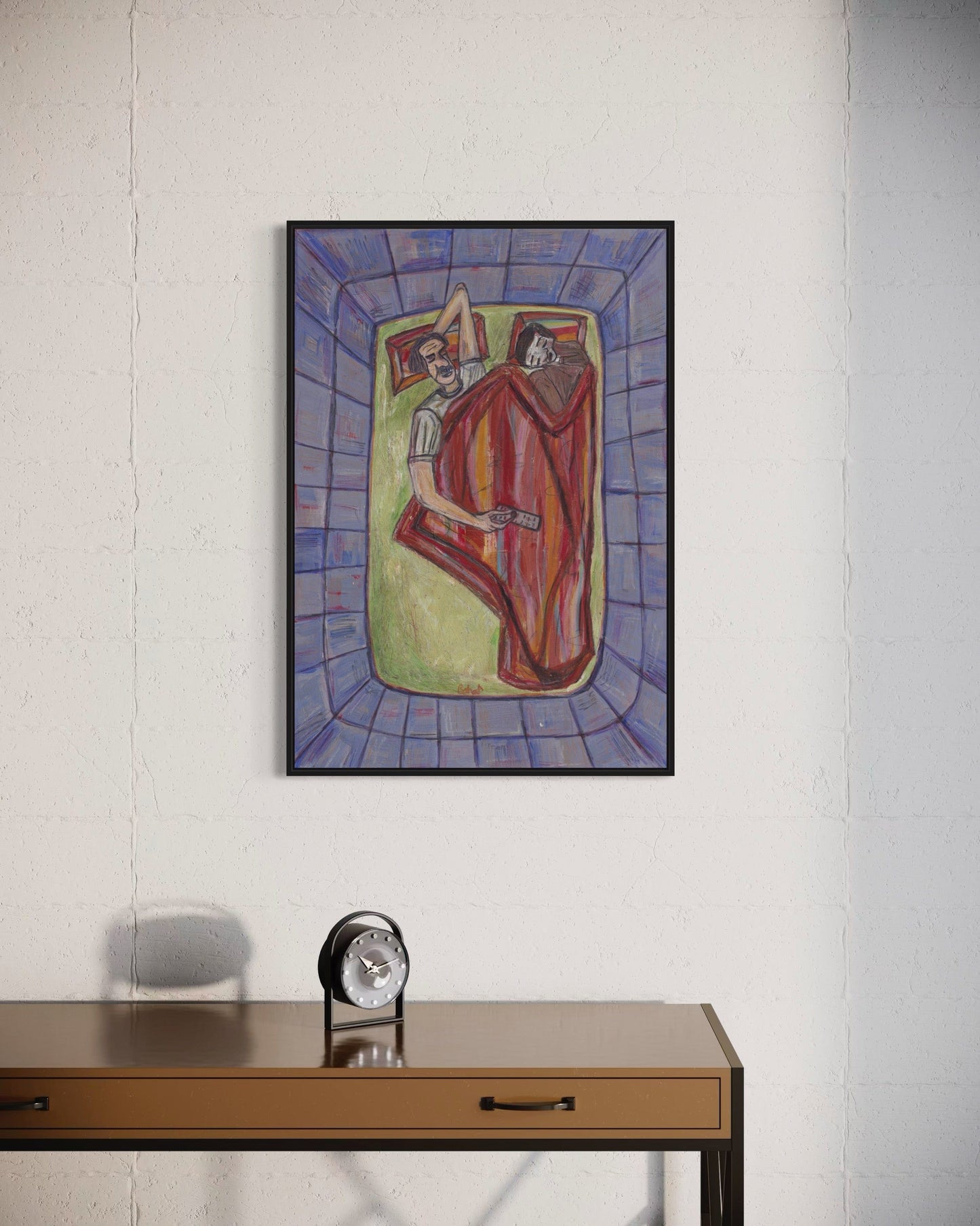 Framed abstract painting on a wall above a wooden desk with a clock.