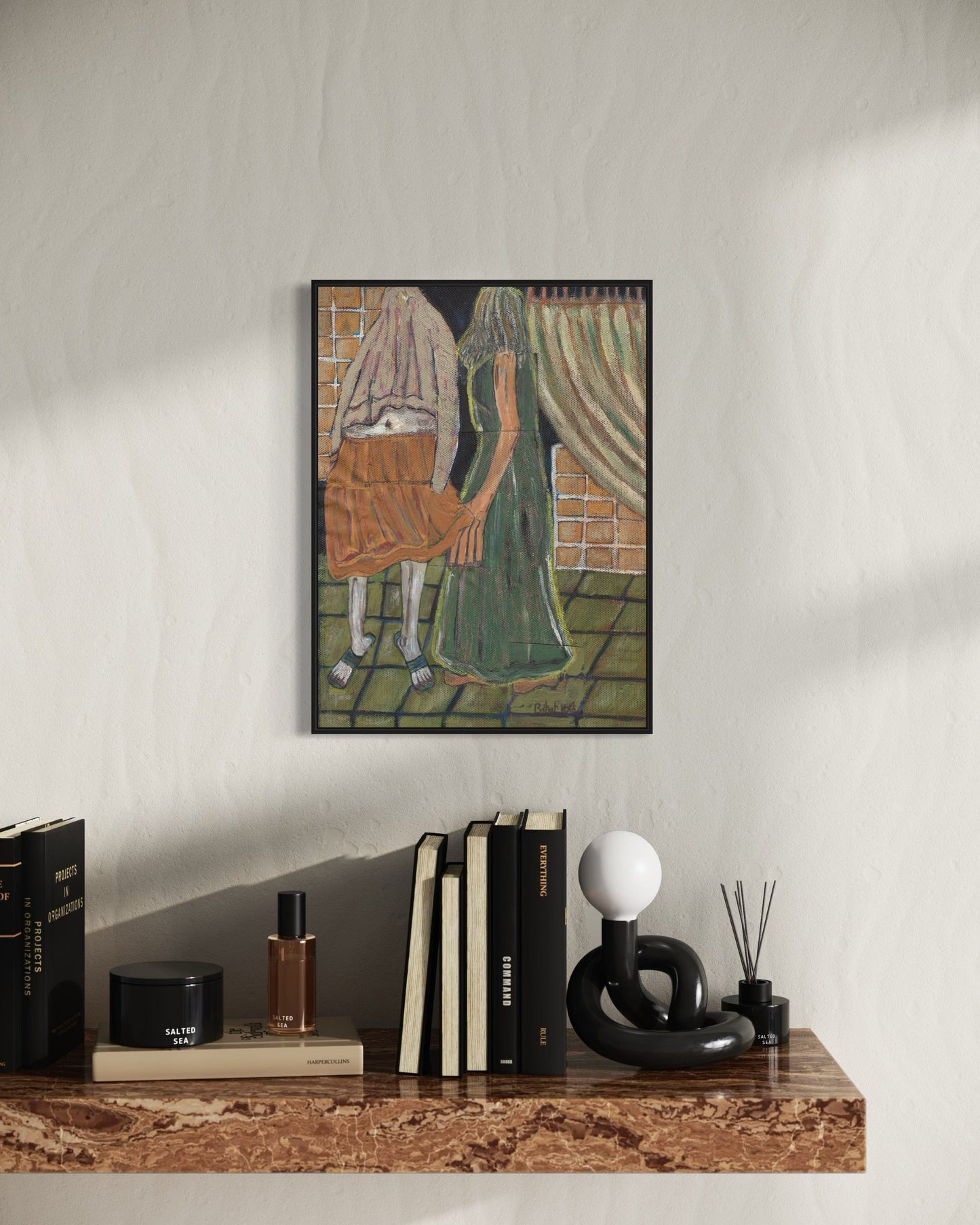 Framed artwork on a wall above a wooden shelf with books and decorative items.