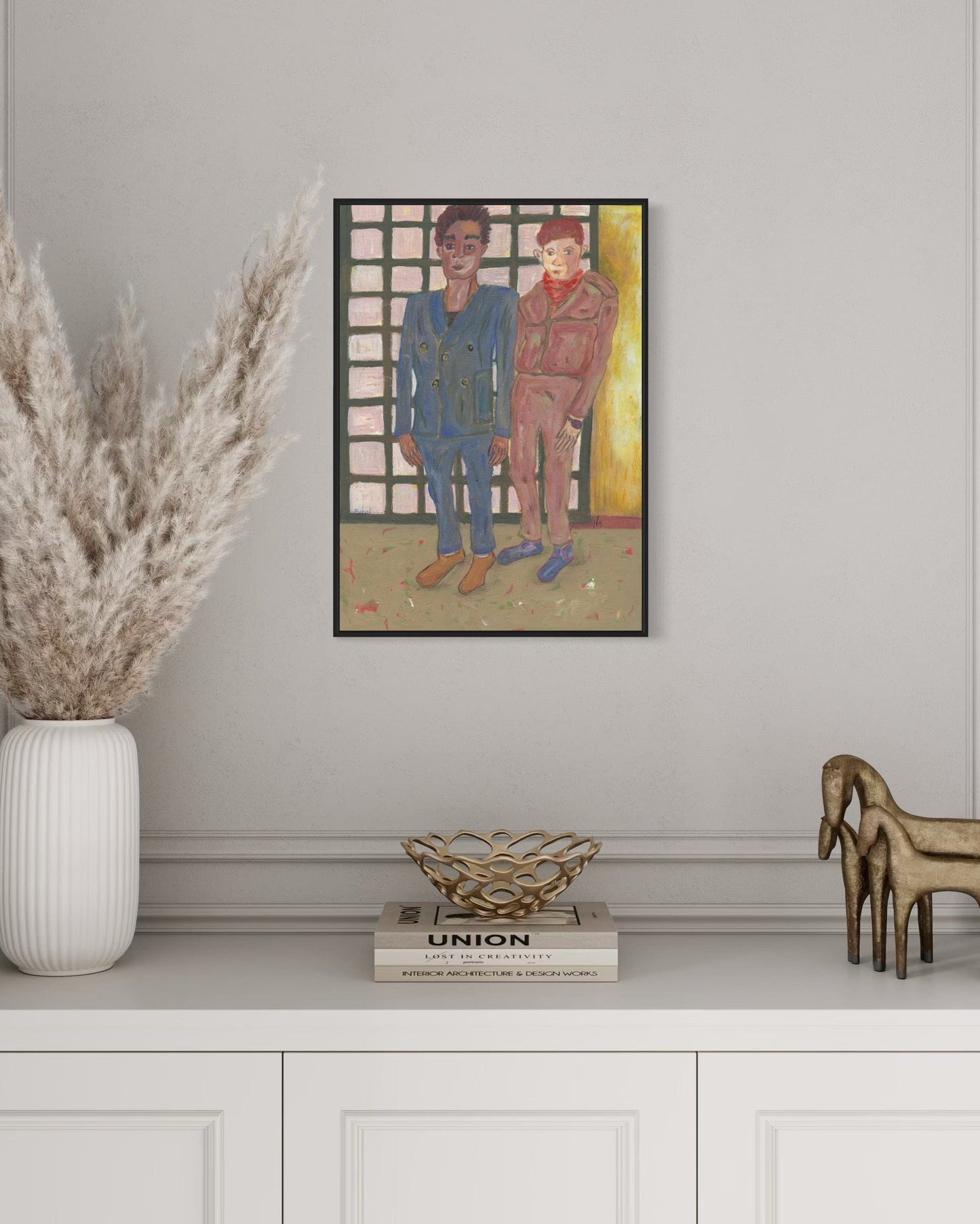 Framed artwork of two people on a wall above a white cabinet with decorative items.