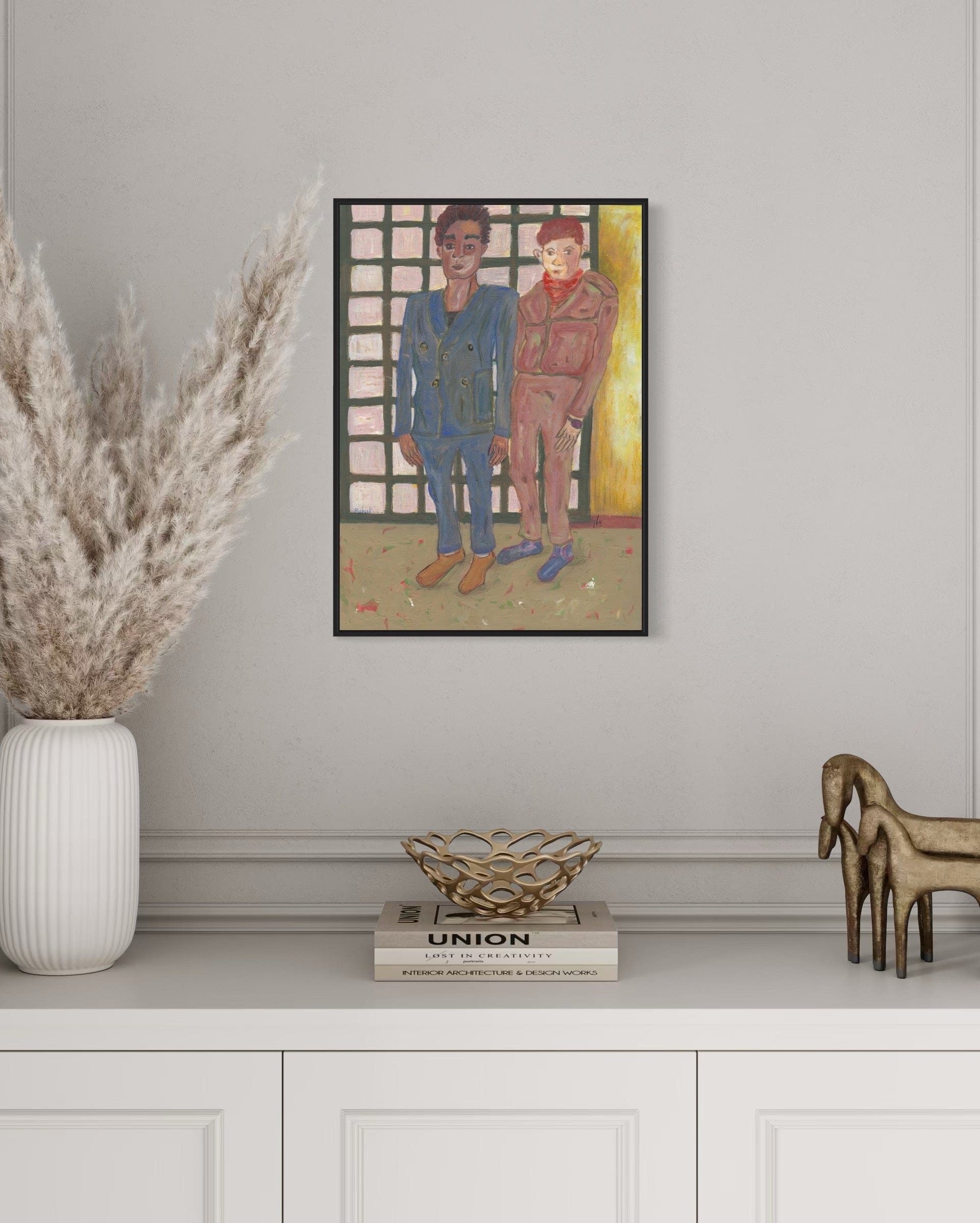 Framed artwork of two people on a wall above a white cabinet with decorative items.