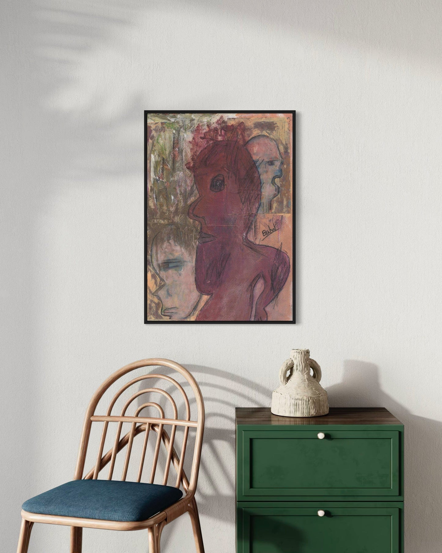 Framed abstract art piece on a wall above a chair and green cabinet.