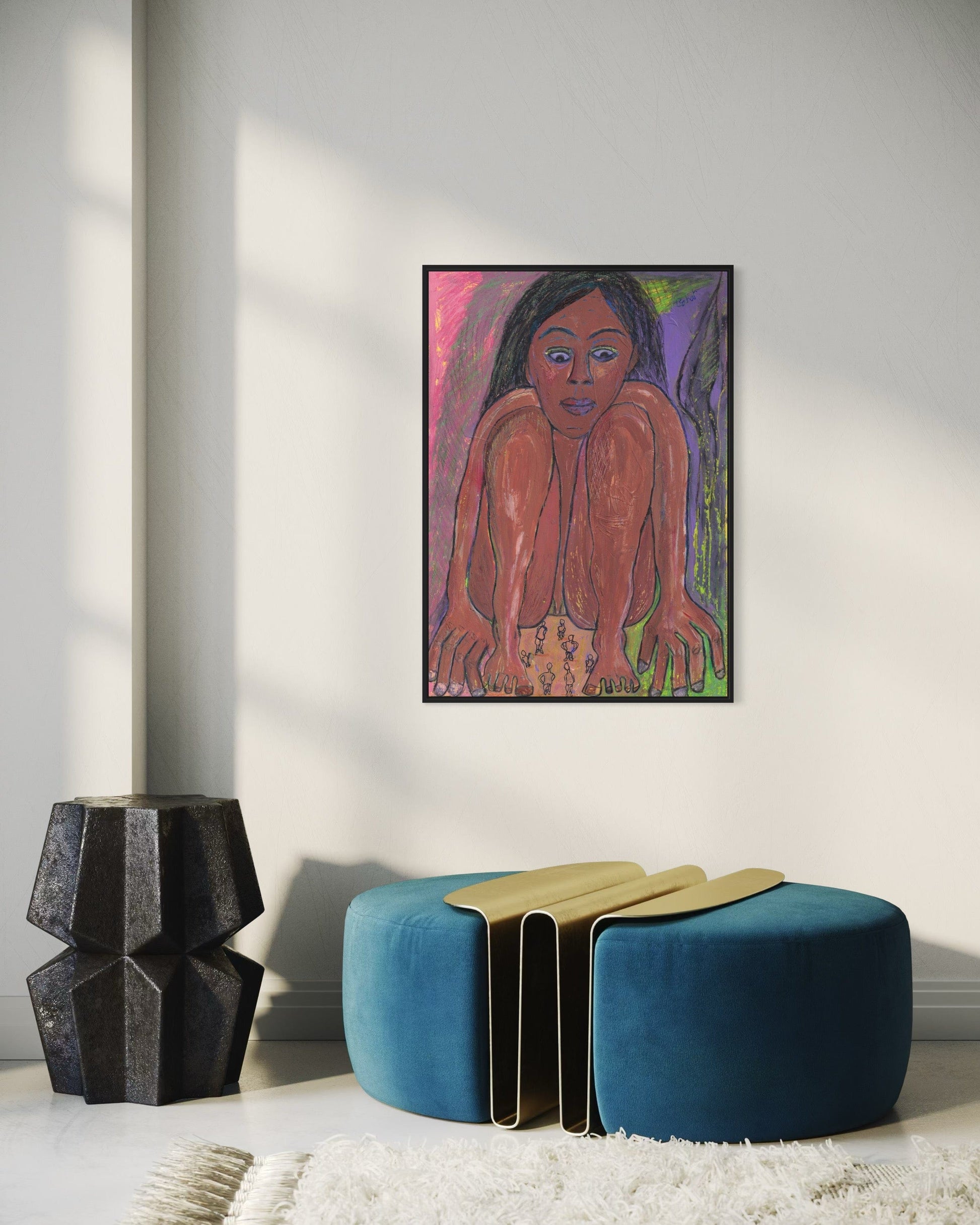 Framed artwork of a woman's portrait on a wall with a blue ottoman and black vase below.