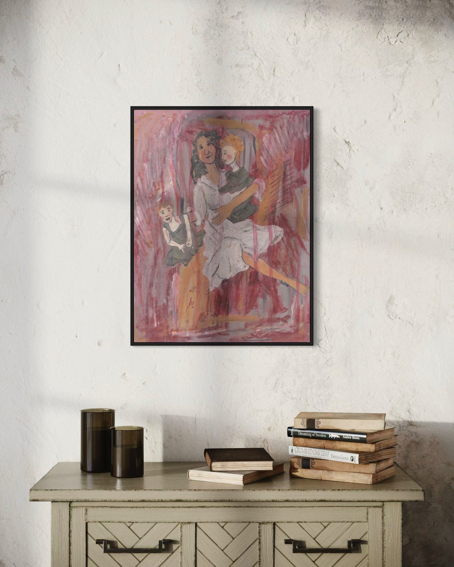 Framed artwork of three people on a wall above a wooden cabinet with books.