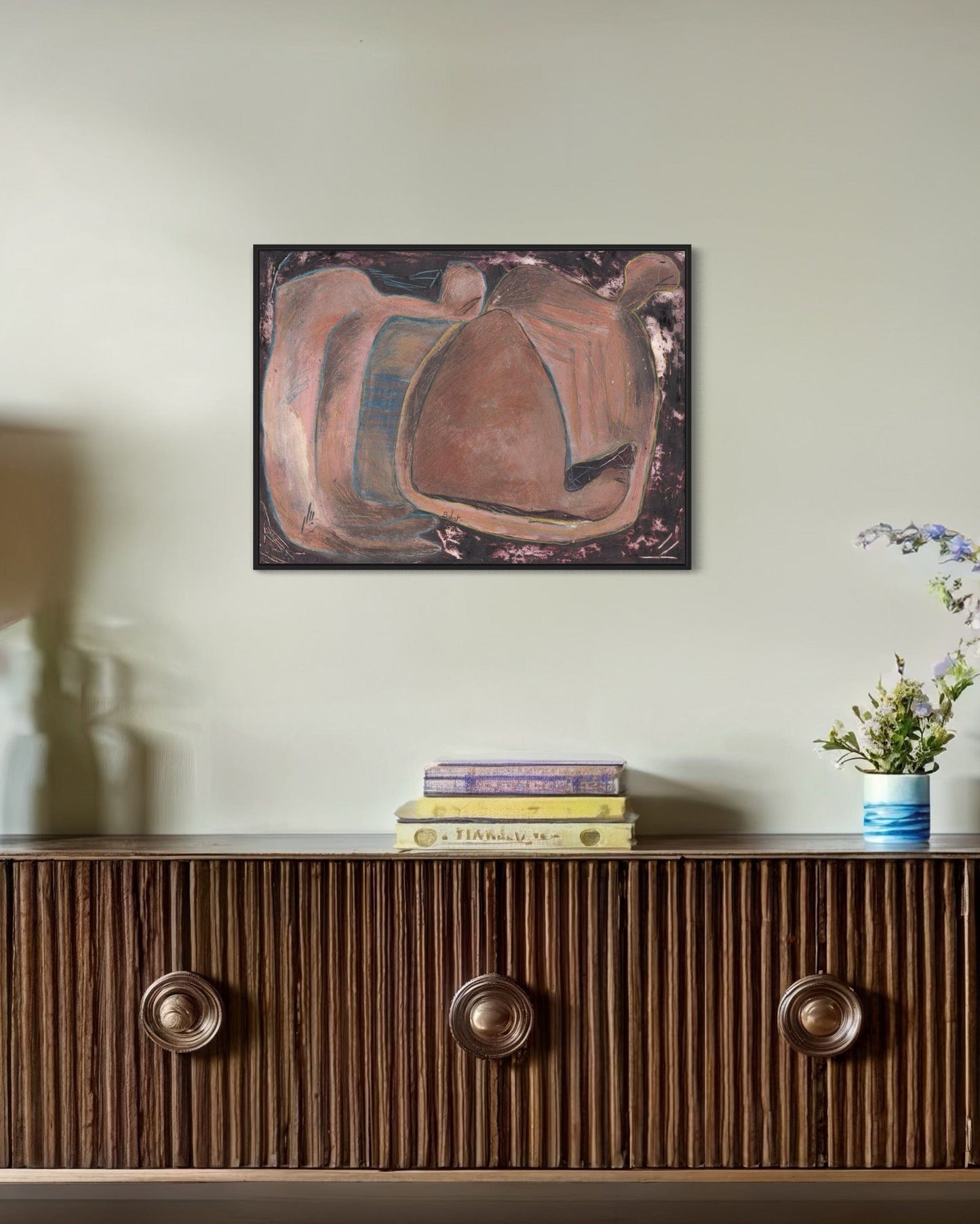 Abstract painting on a wall above a wooden console table with books and a vase.